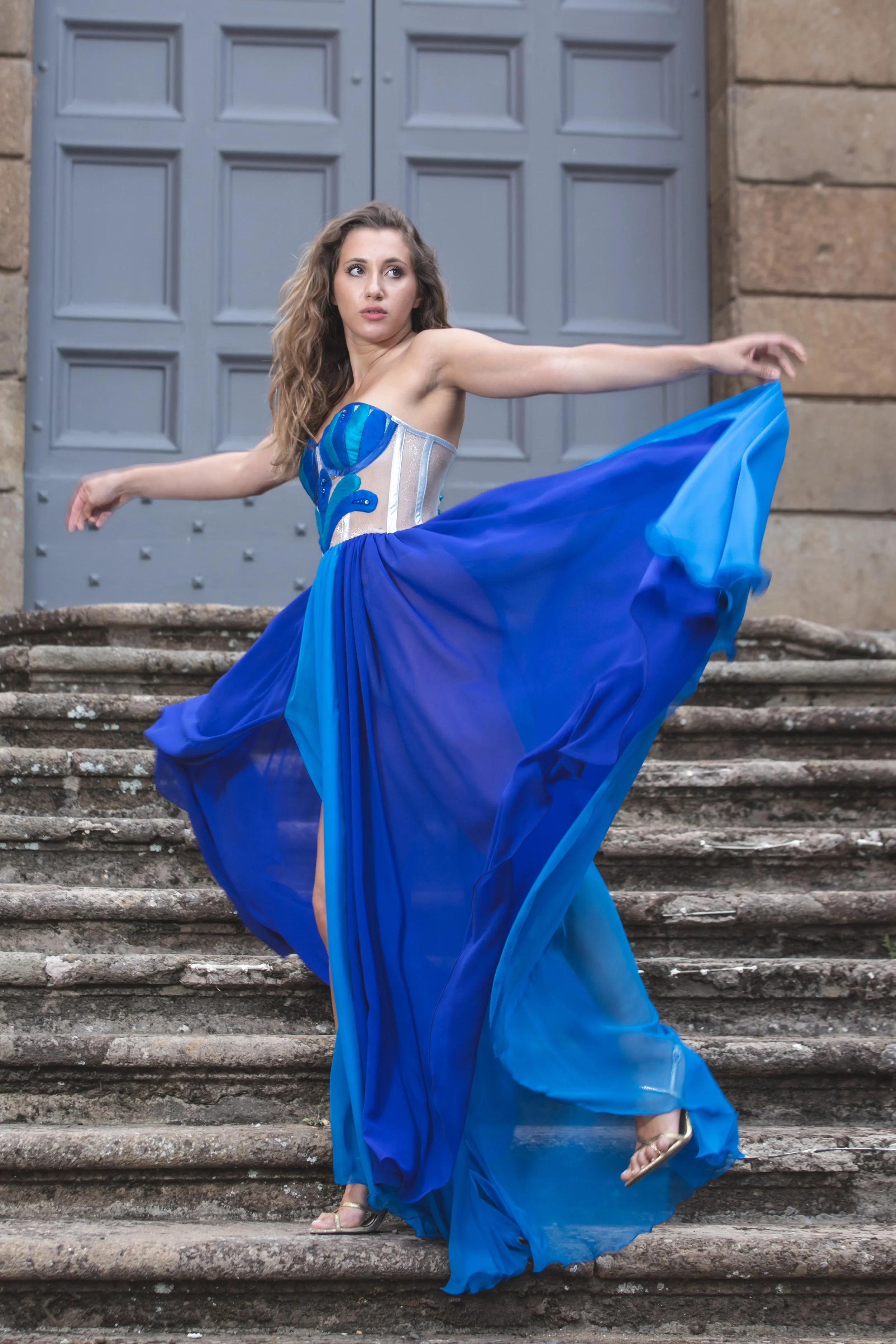 corpino realizzato in nylon laminato argento con gocce realizzate a mano in shantung nei toni del blu –azzurro. Le gocce sono ricamate a mano con Swarovski e perline blu e azzurre.
Gonna con spacco laterale in chiffon azzurro e blu.
