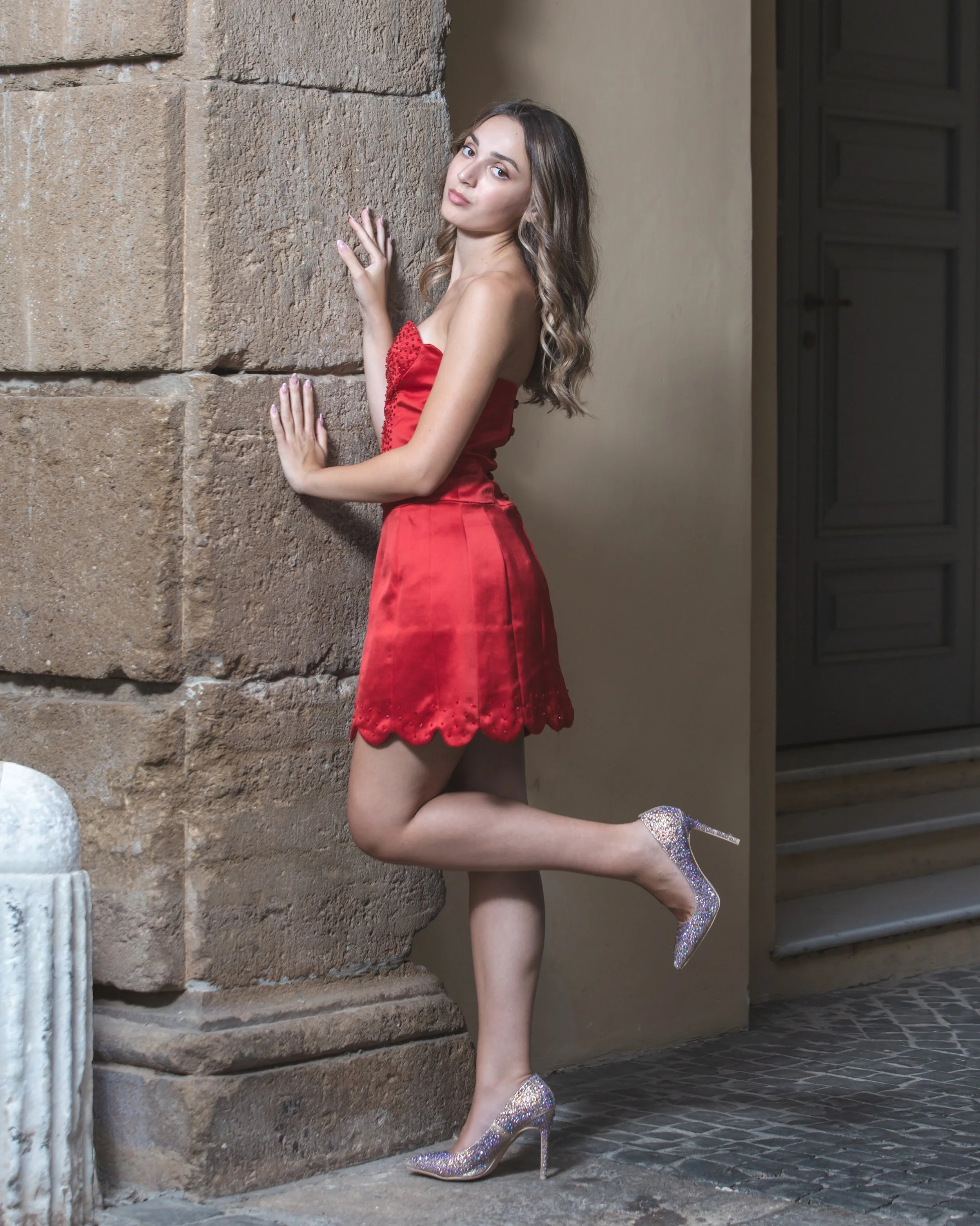 Mini abito realizzato in pannelli di raso rosso. Scollo a cuore con profonda scollatura sul davanti ricamata in Swarovski rossi. La gonna ha un orlo smerlato con ricami sul fondo. 
