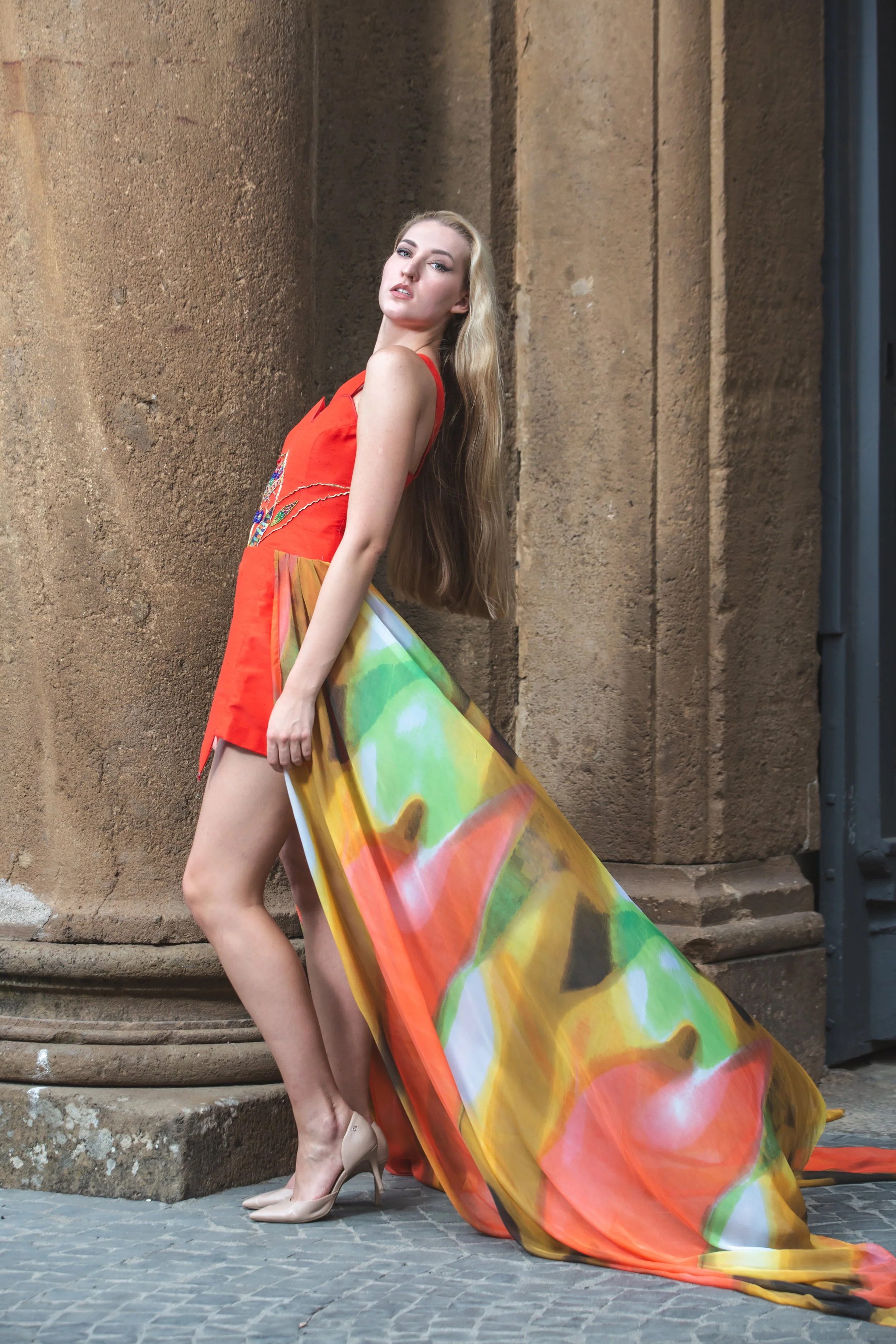 abito mono spalla realizzato in shantung rosso. Sul busto si notano ricami realizzati a mano con perline colorate, strass, filo e soutage dorata. Gonna composta da pannelli di stoffa cuciti insieme con orli a punta (con pendenti a goccia). In vita è 