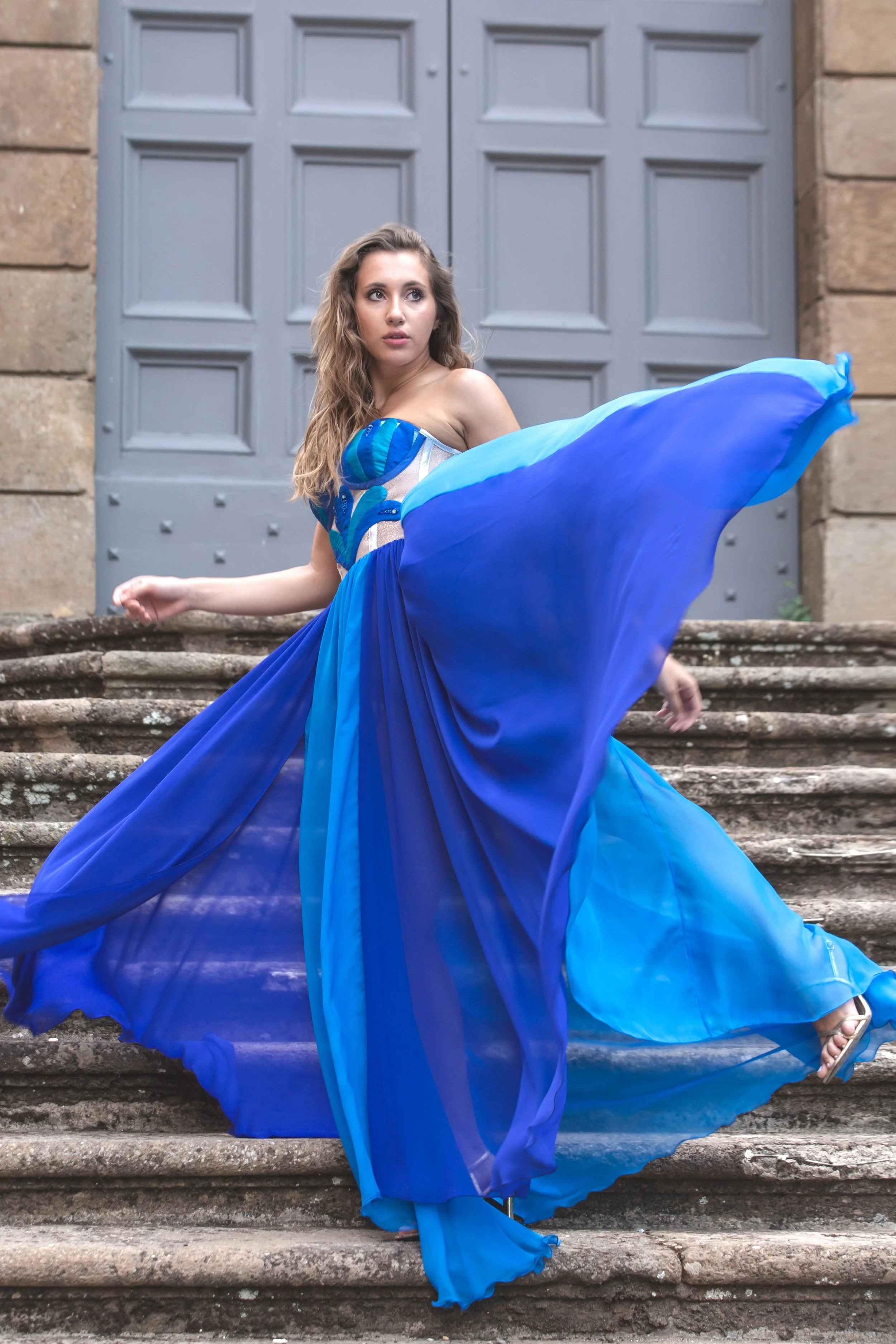 corpino realizzato in nylon laminato argento con gocce realizzate a mano in shantung nei toni del blu –azzurro. Le gocce sono ricamate a mano con Swarovski e perline blu e azzurre.
Gonna con spacco laterale in chiffon azzurro e blu.
