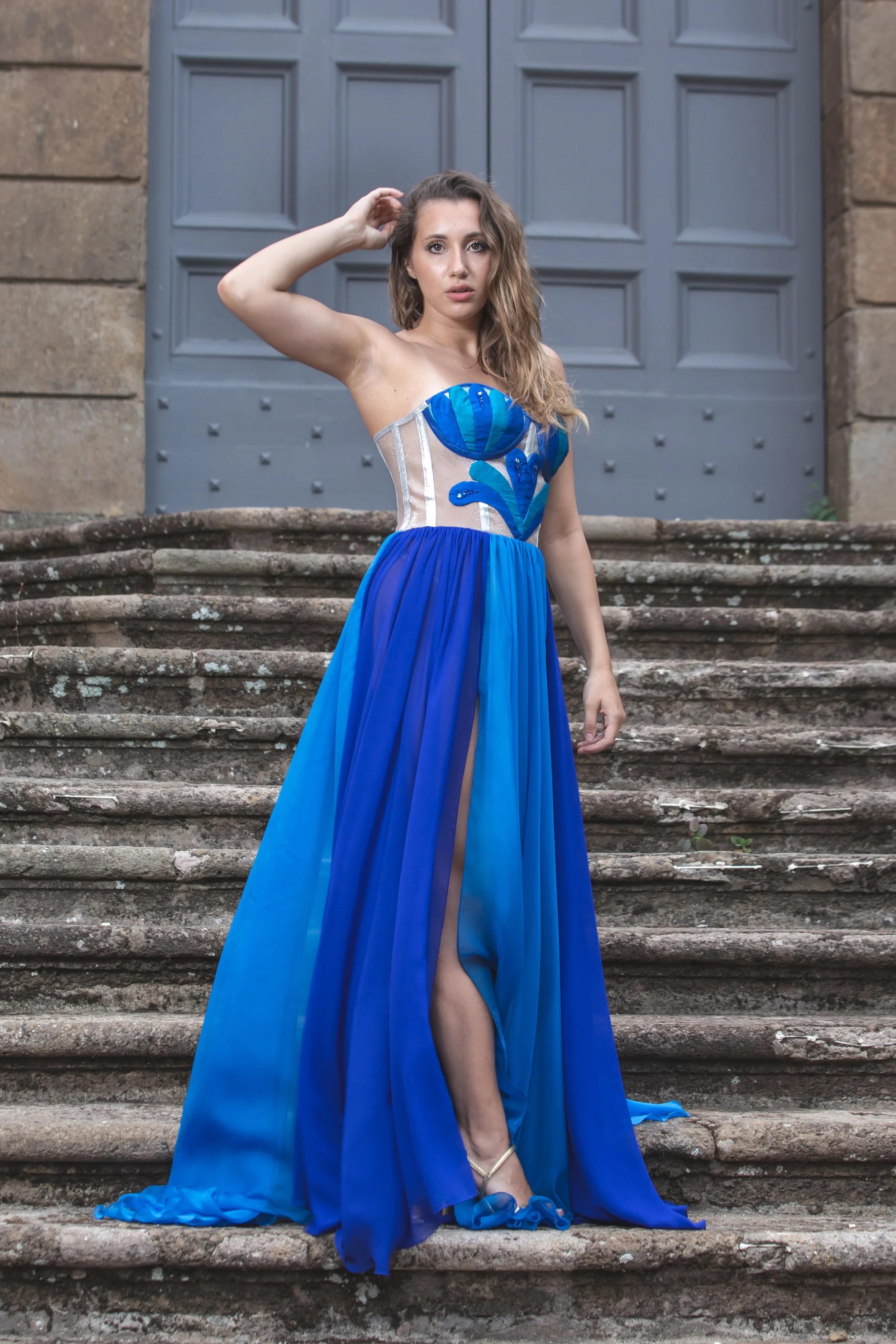 corpino realizzato in nylon laminato argento con gocce realizzate a mano in shantung nei toni del blu –azzurro. Le gocce sono ricamate a mano con Swarovski e perline blu e azzurre.
Gonna con spacco laterale in chiffon azzurro e blu.
