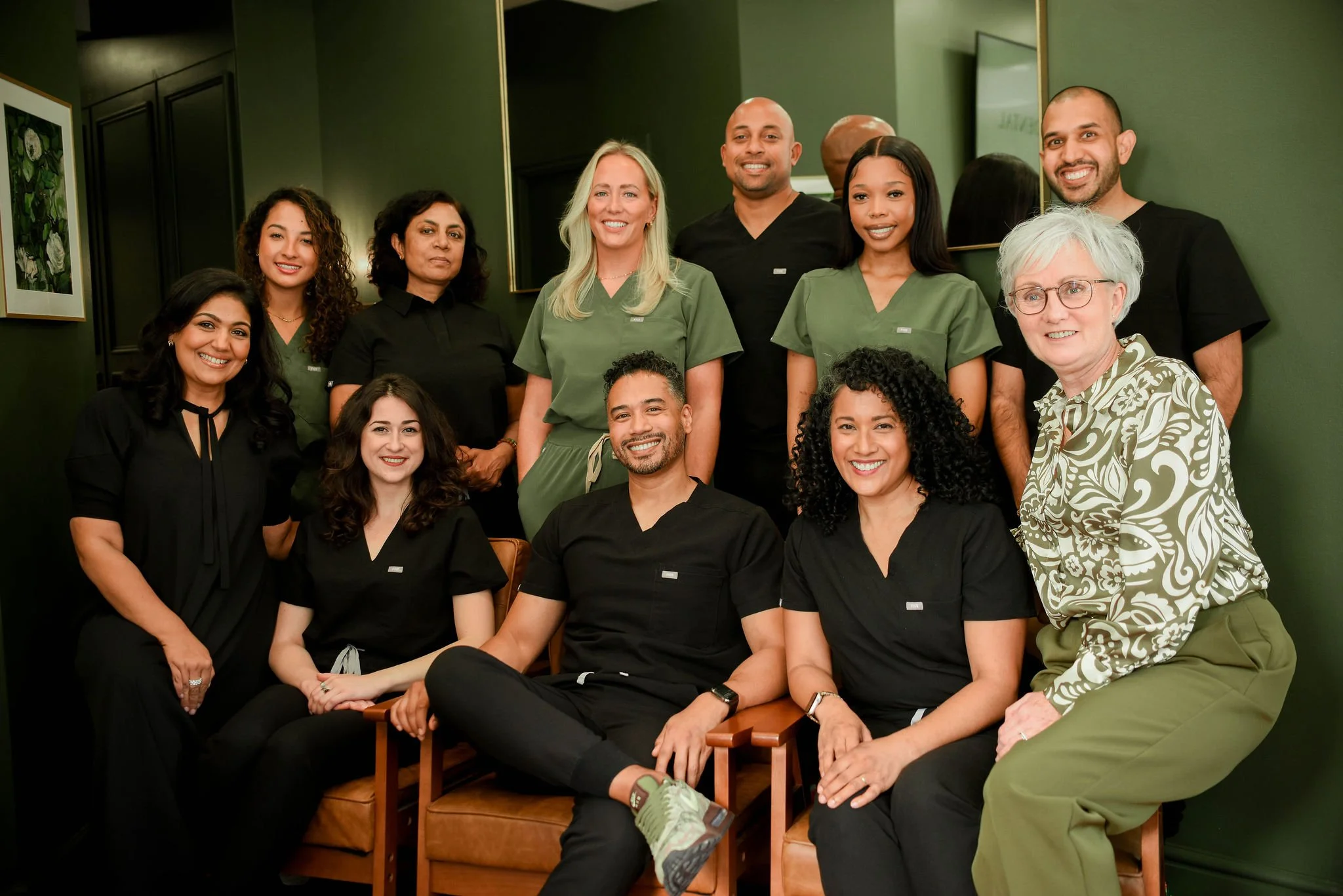 Group of healthcare professionals, including men and women of diverse ethnicities, posing together in a room with green walls and framed artwork.