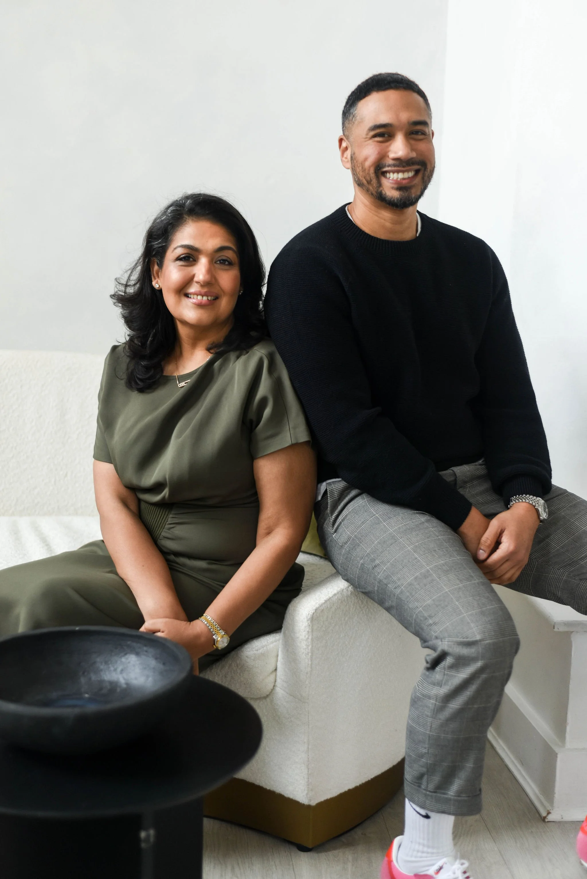 A man and woman sitting together on a white sofa in a room, smiling at the camera.