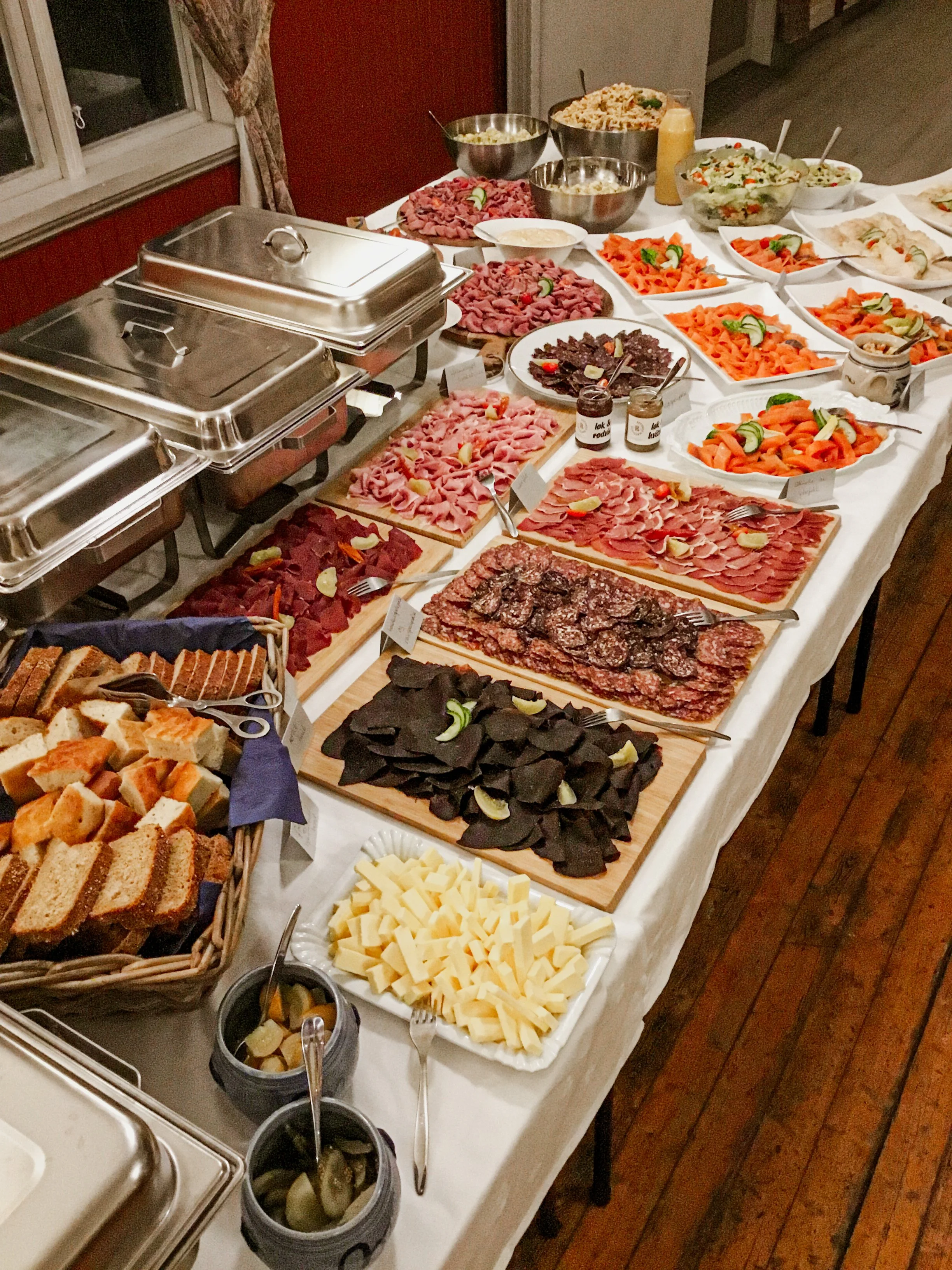 Buffet med kjøttpålegg, laks, brød og beholdere med varm mat.