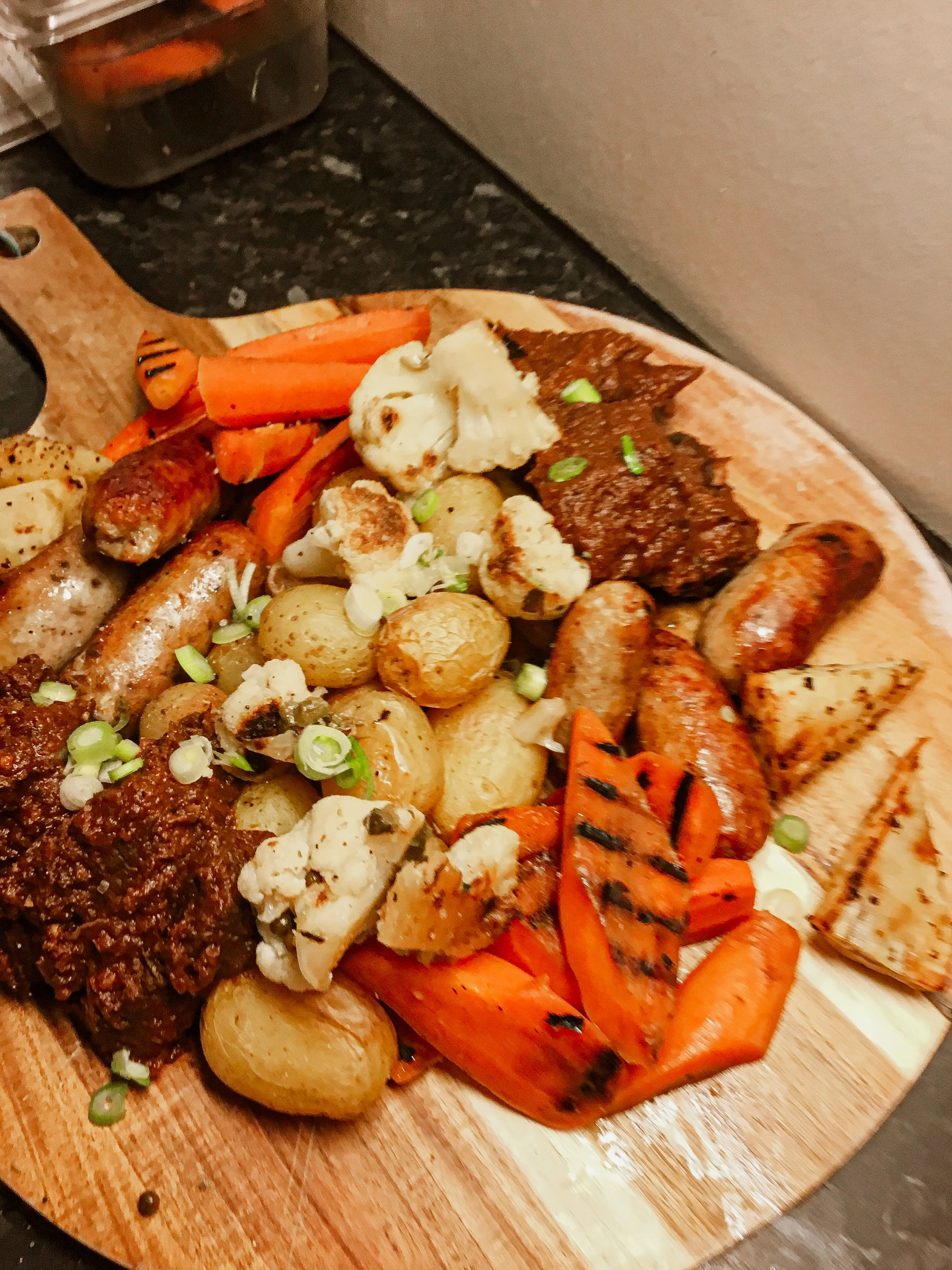 Nærbilde av småpoteter med skall, pølser, grilla gulerøtter, blomkål med mer.