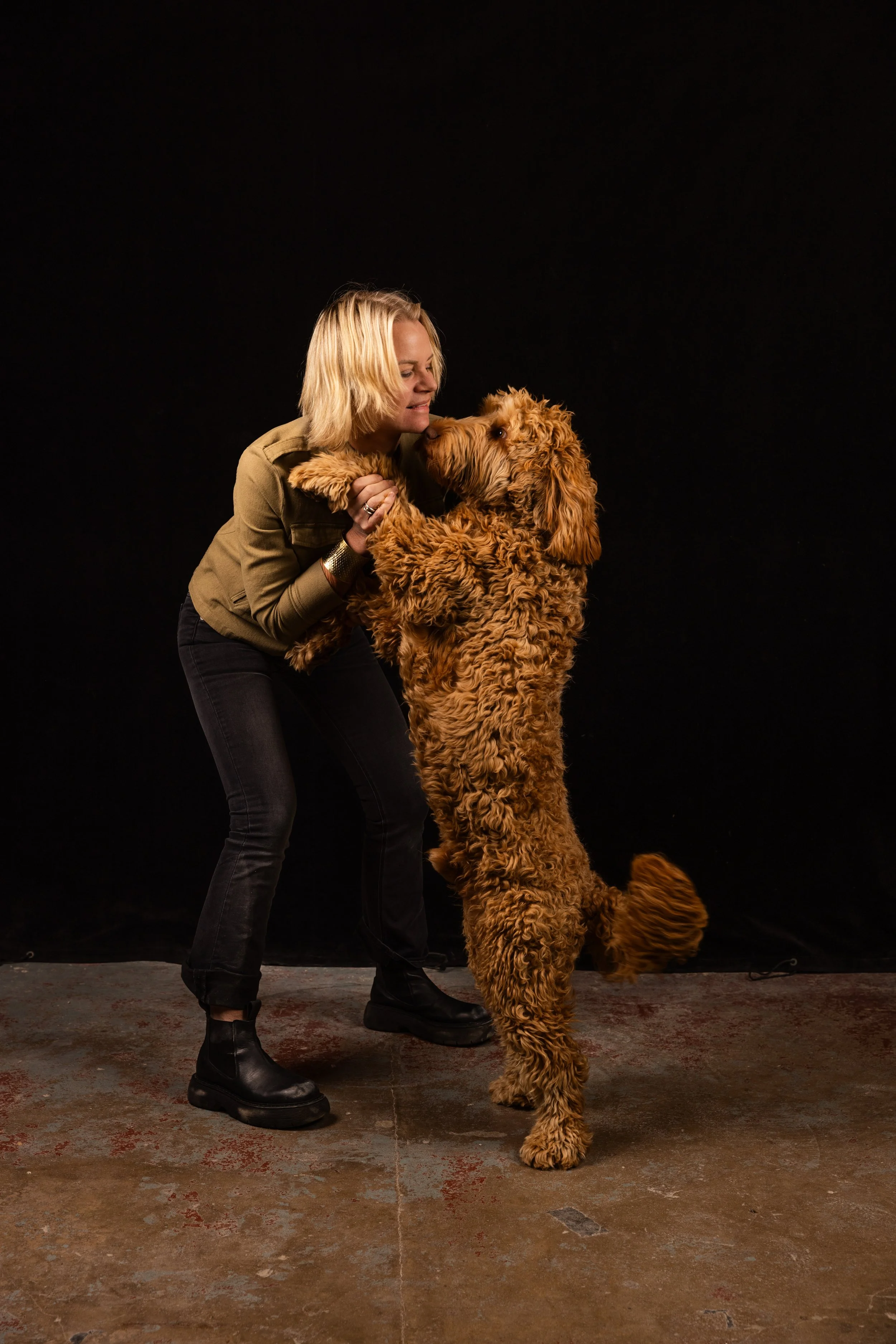 A woman holding the paws of a large curly-haired dog in a studio.