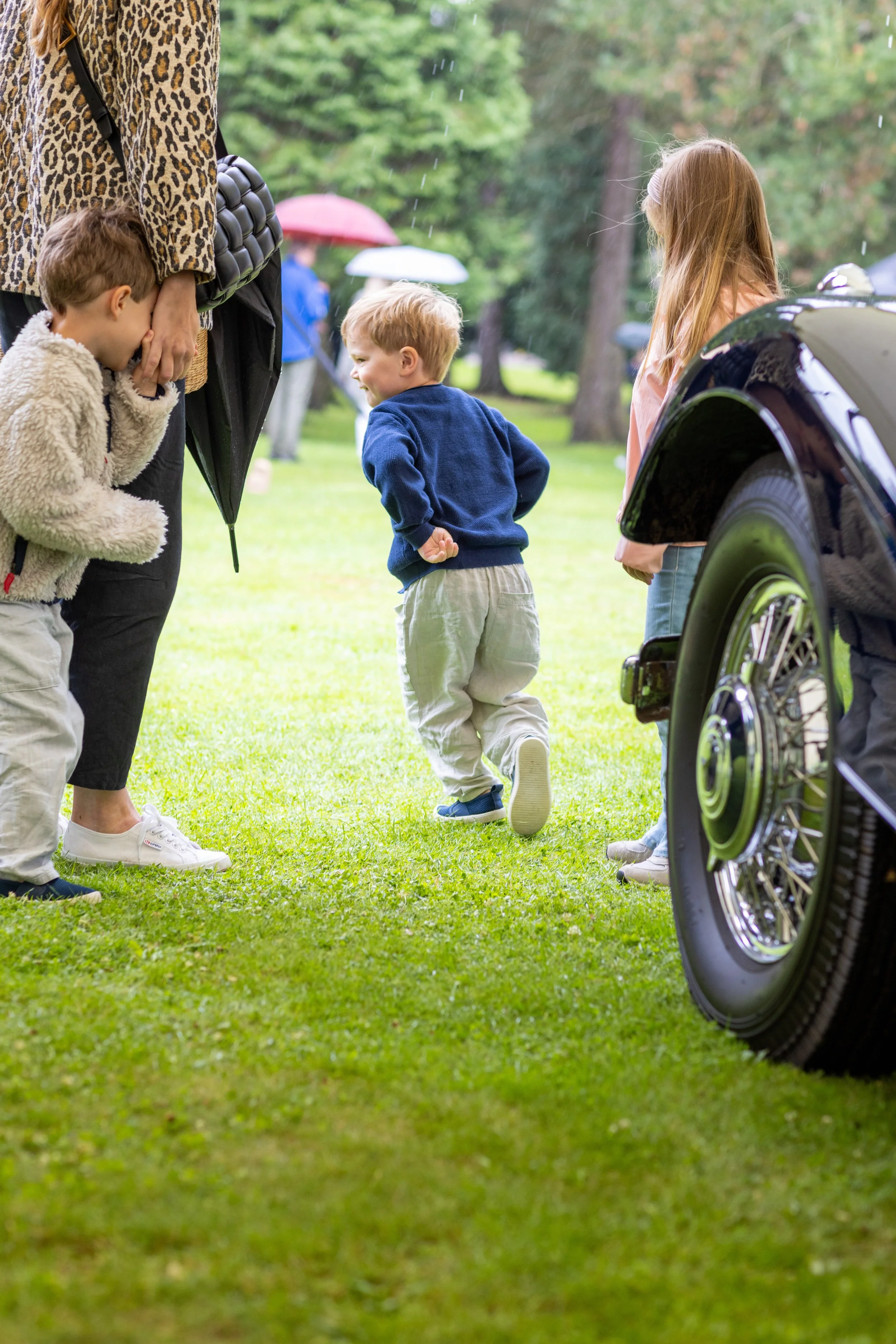 Children standing on grass beside a vintage car.