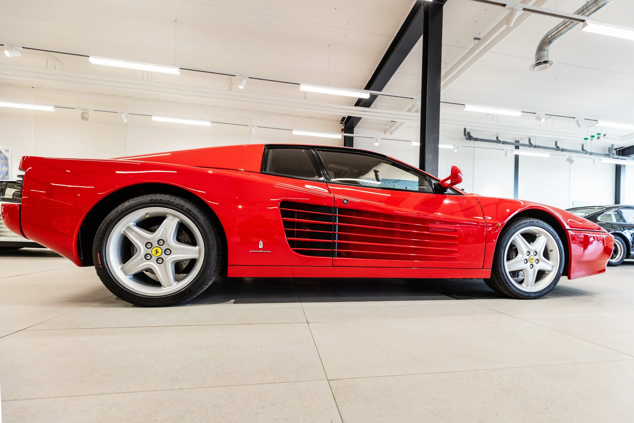 A red Ferrari photographed from the side inside a showroom.