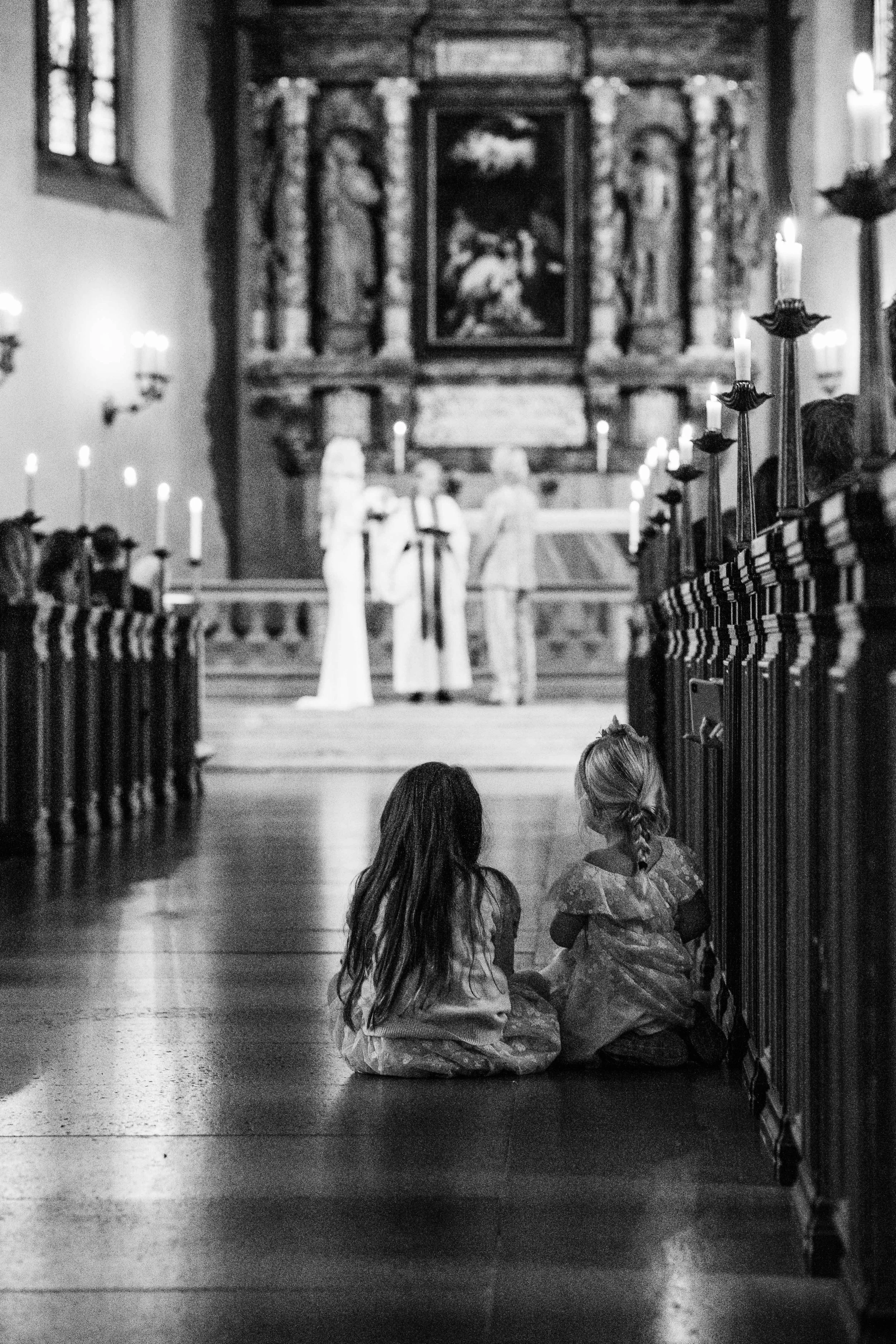 Two children sitting in a church aisle during a wedding ceremony.