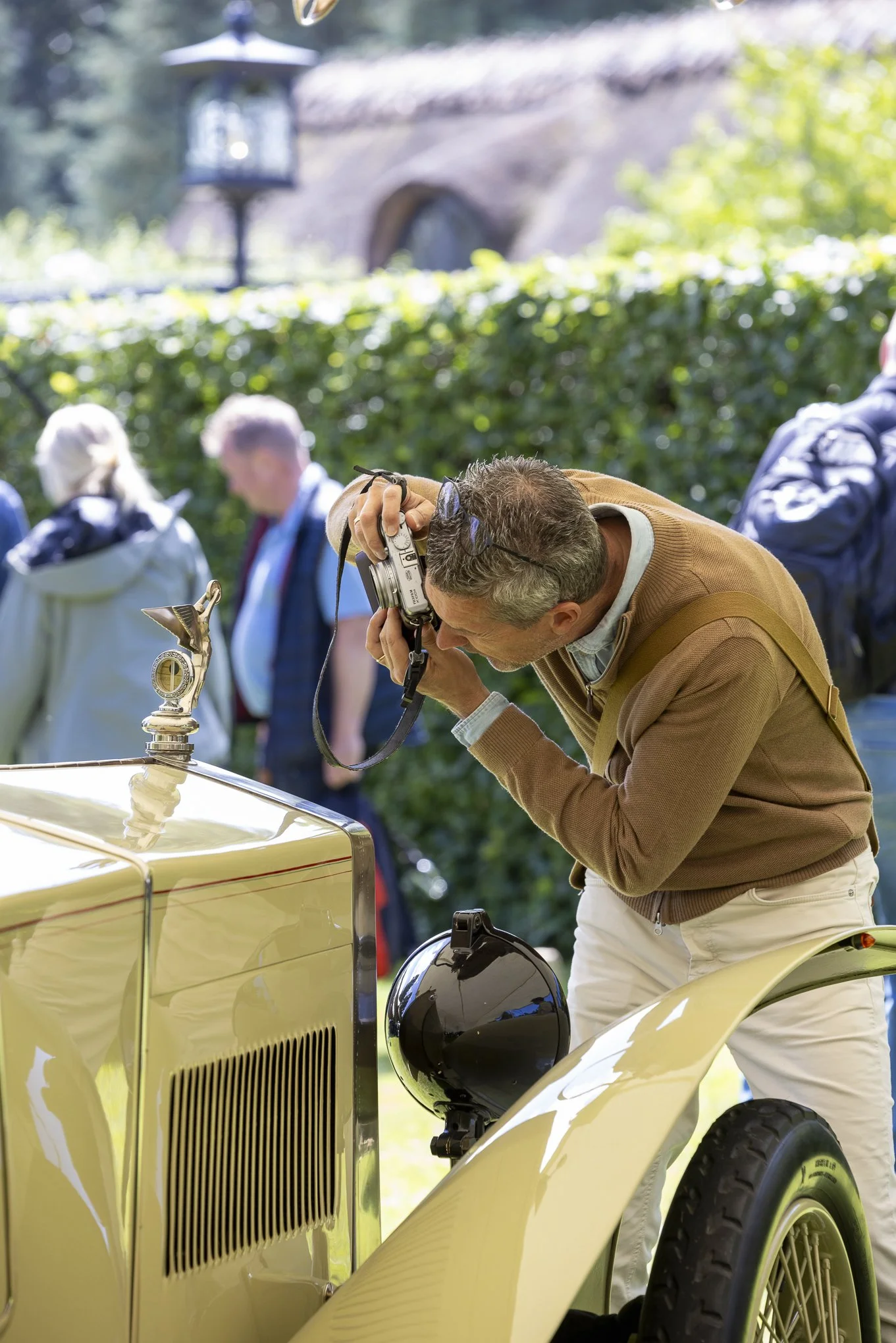 A photographer taking a close-up photograph of a yellow vintage car.