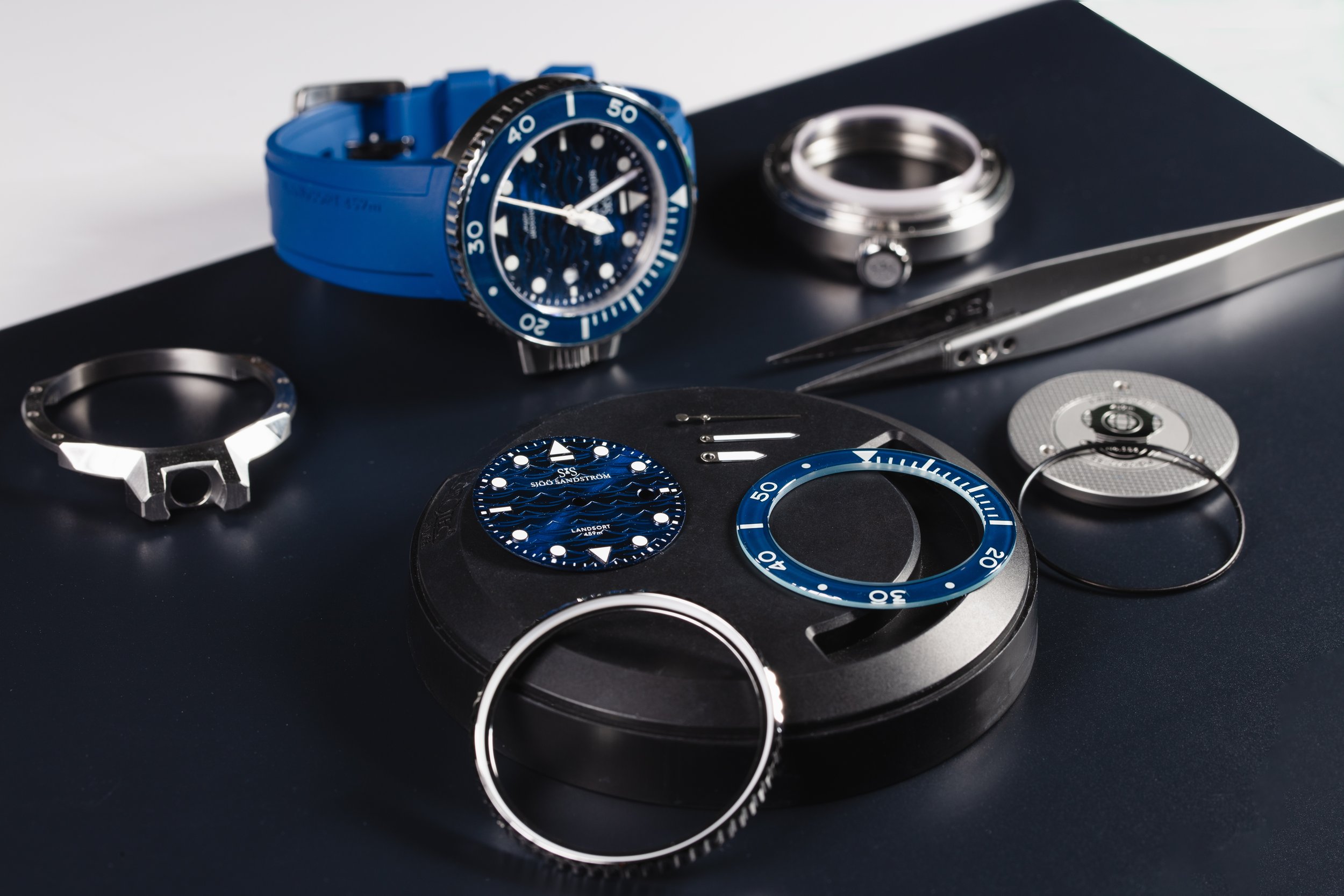 A blue Sjöö Sandström wristwatch displayed with its dial, bezel and case components.