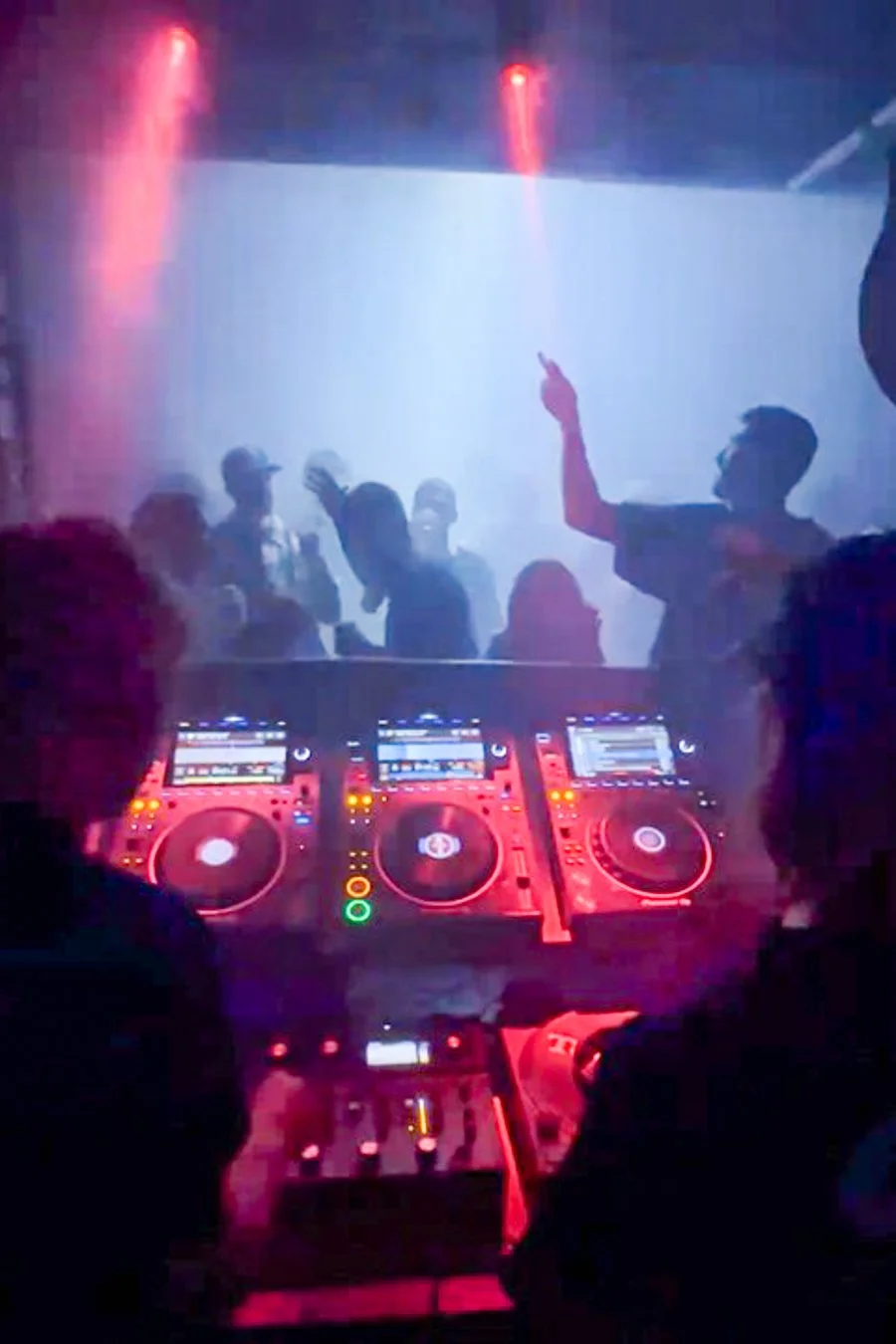 A DJ performing behind a mixing desk with dancers and coloured lights.