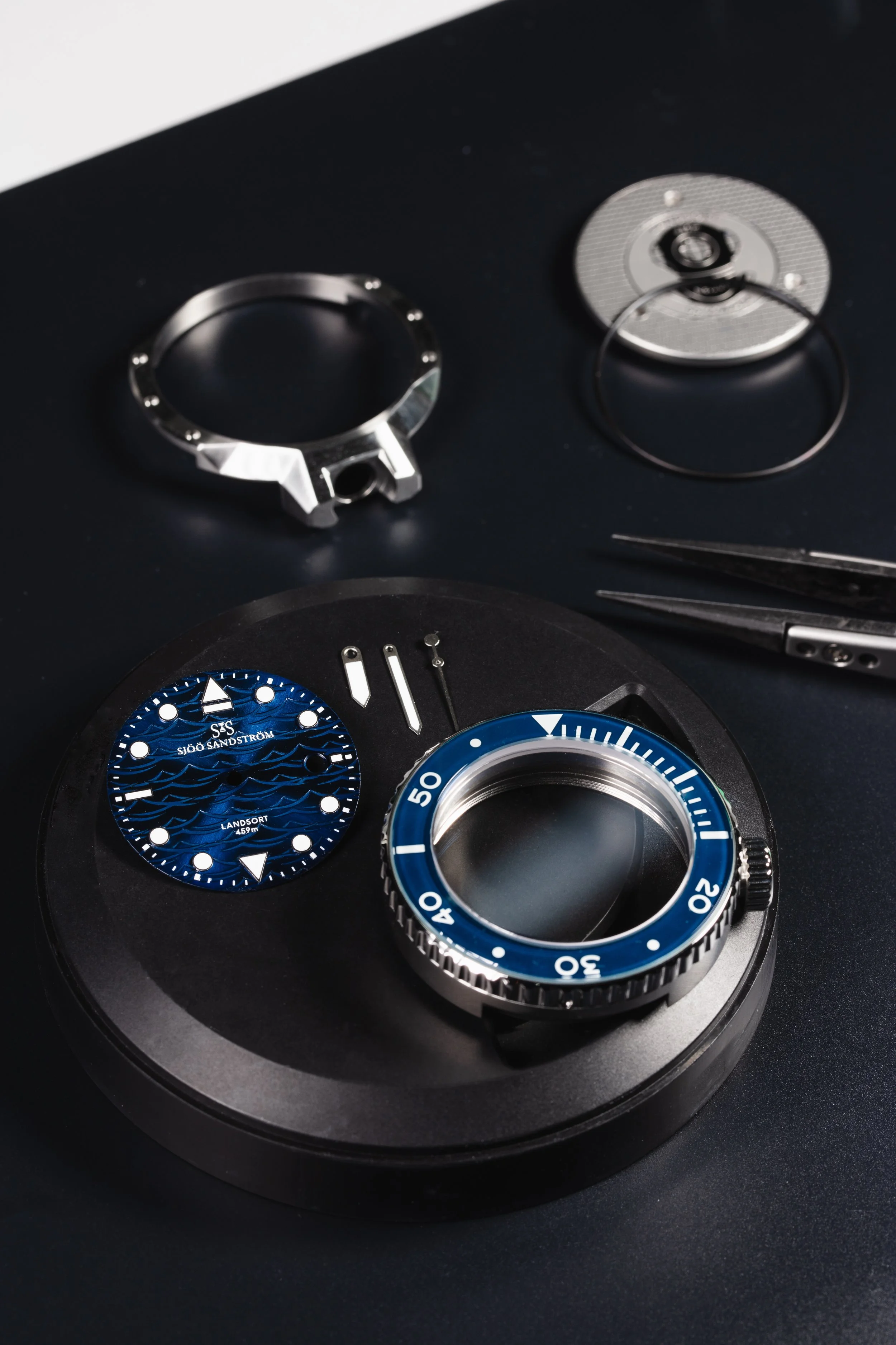 Sjöö Sandström watch components with a blue dial and bezel on a dark work surface.