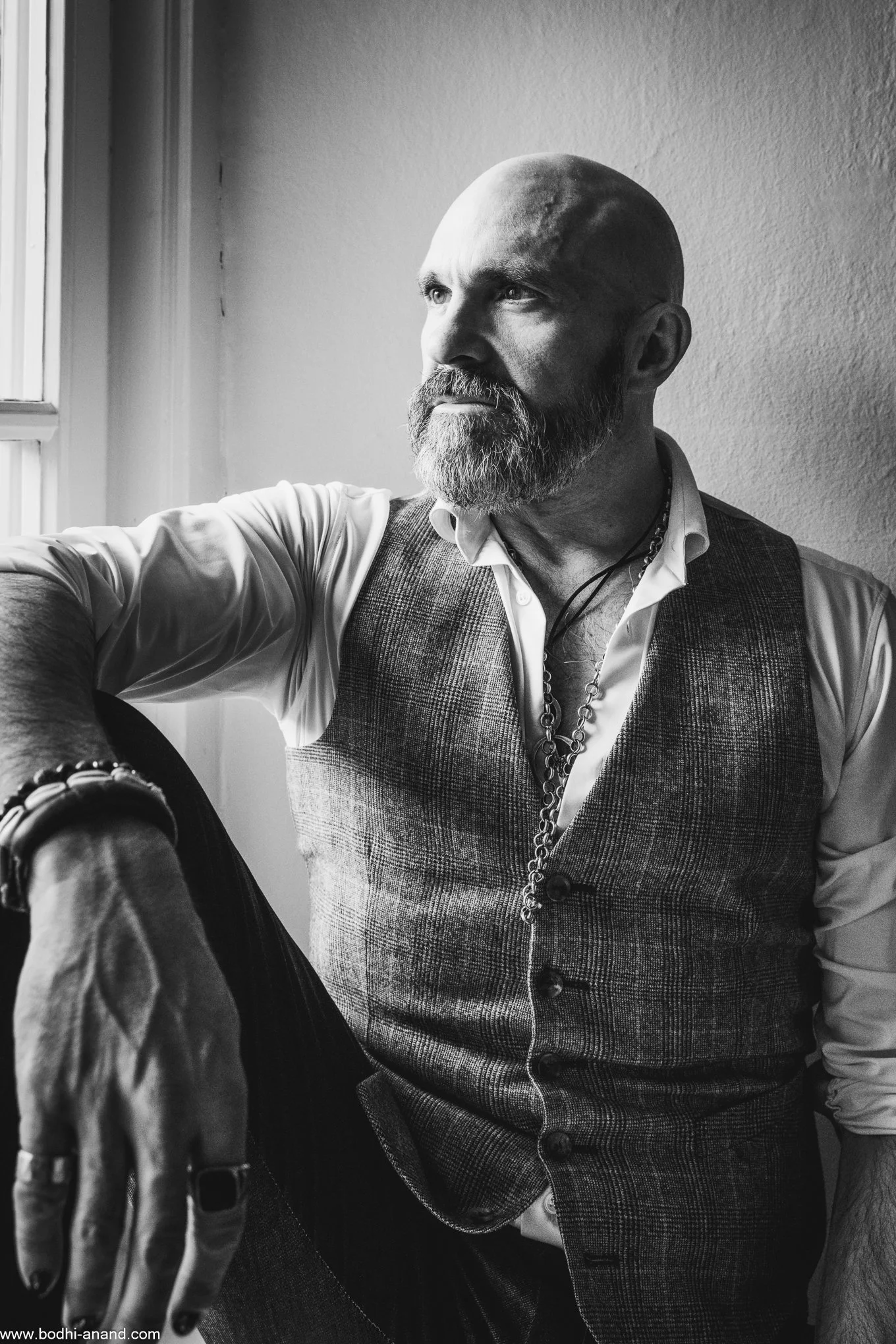 Black-and-white portrait of a bearded man sitting beside a window.
