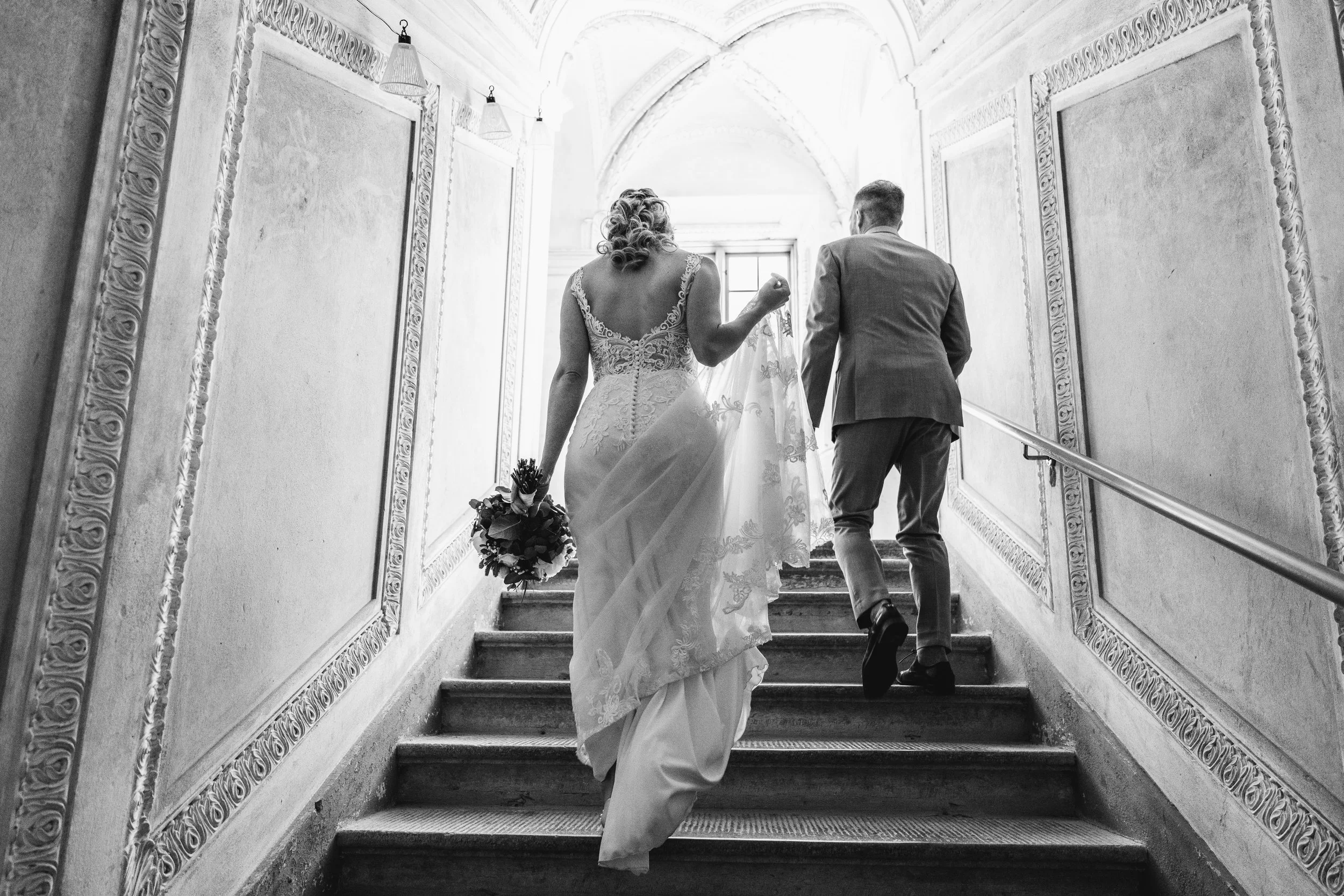 Bride and groom walking up a staircase, photographed in black and white.