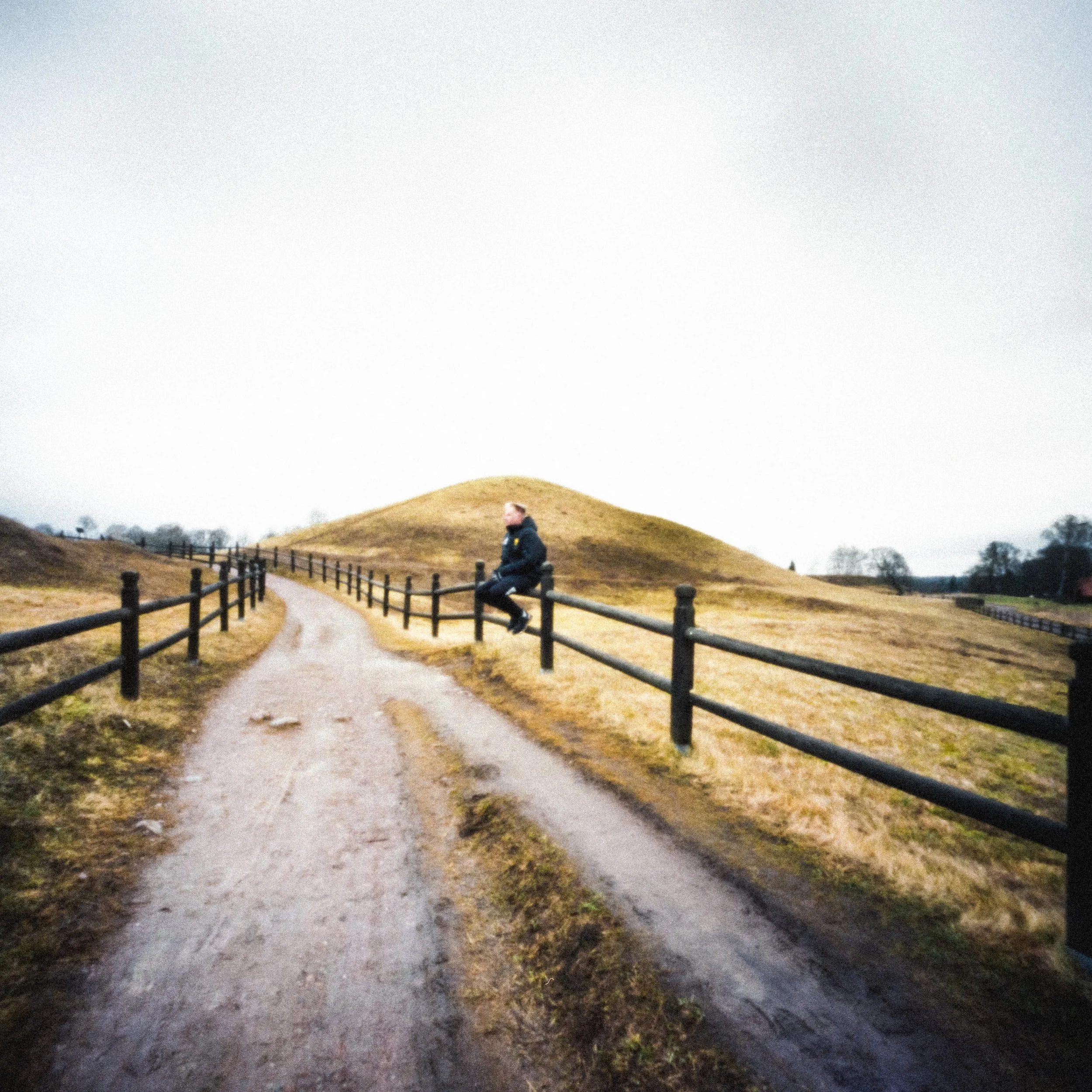A person sitting beside a country path in open countryside.
