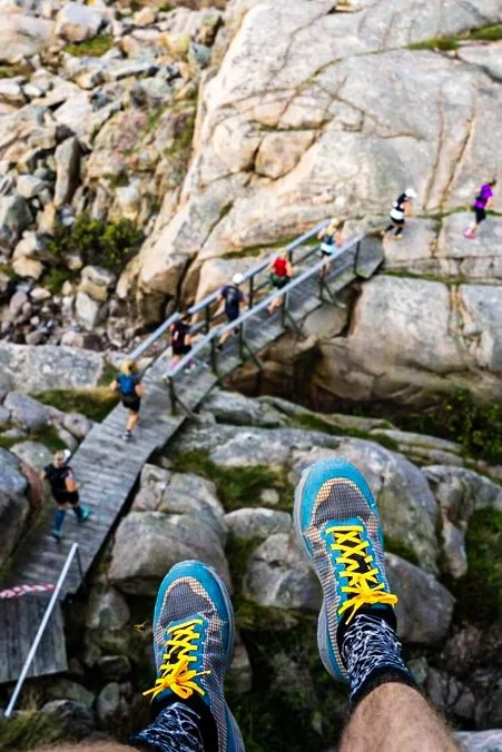 A runner’s shoes overlooking a rocky footbridge and people on a trail.