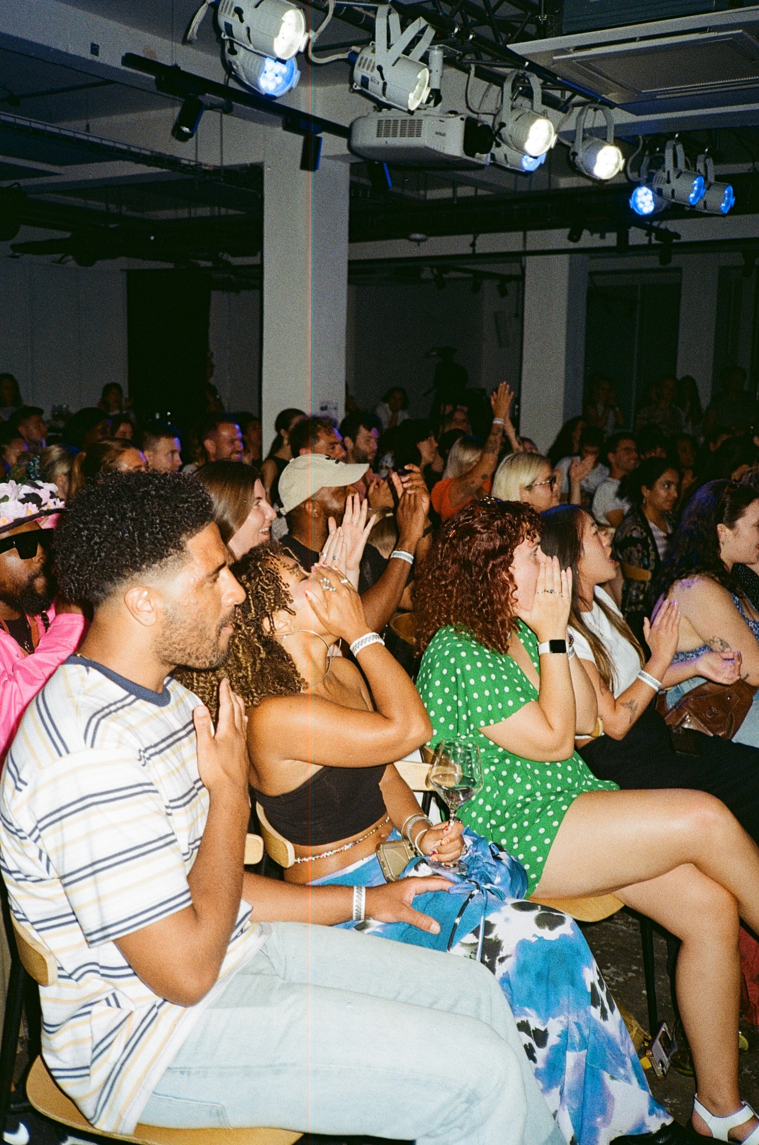 Audience at a concert or event, with some people holding their hands over their hearts, others taking photos, and many reacting emotionally.