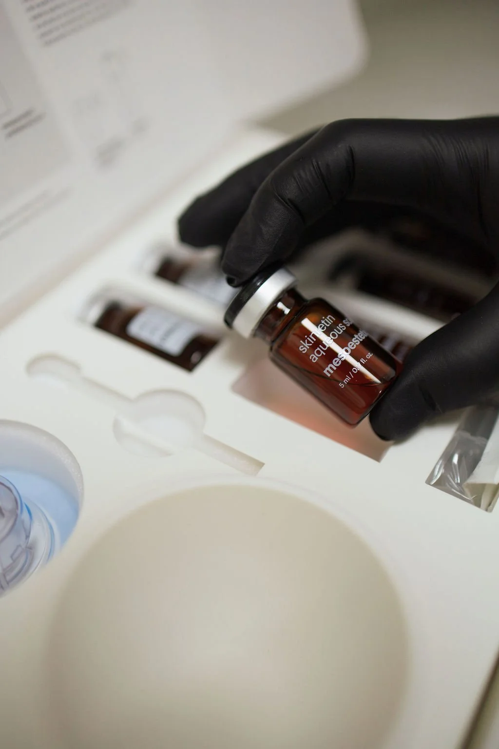 Close-up of a hand in a black glove holding a small brown vial labeled 'skin tretin' and 'melanose'.