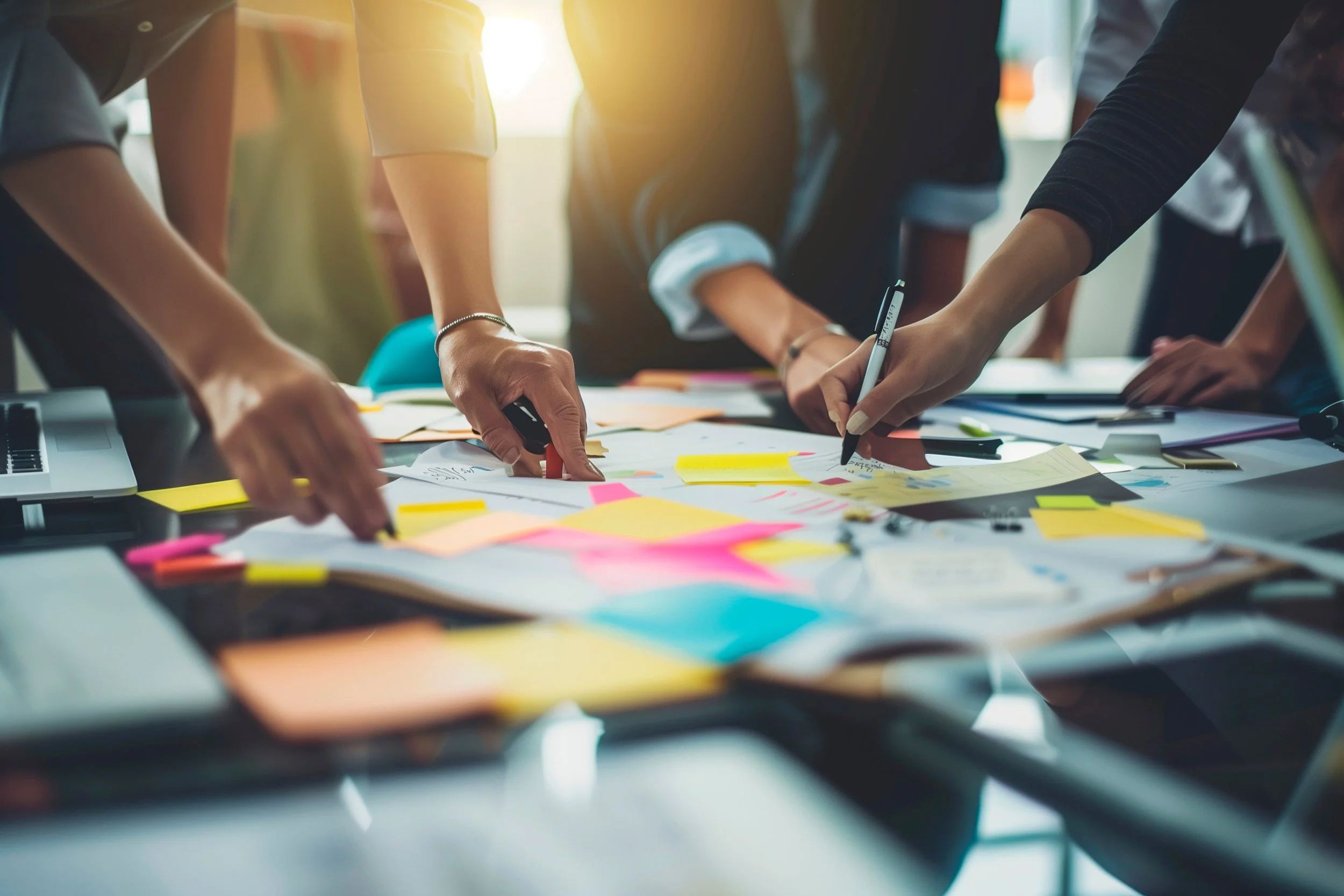 People working together at a table covered with papers, sticky notes, and markers, engaging in a collaborative brainstorming or planning session.