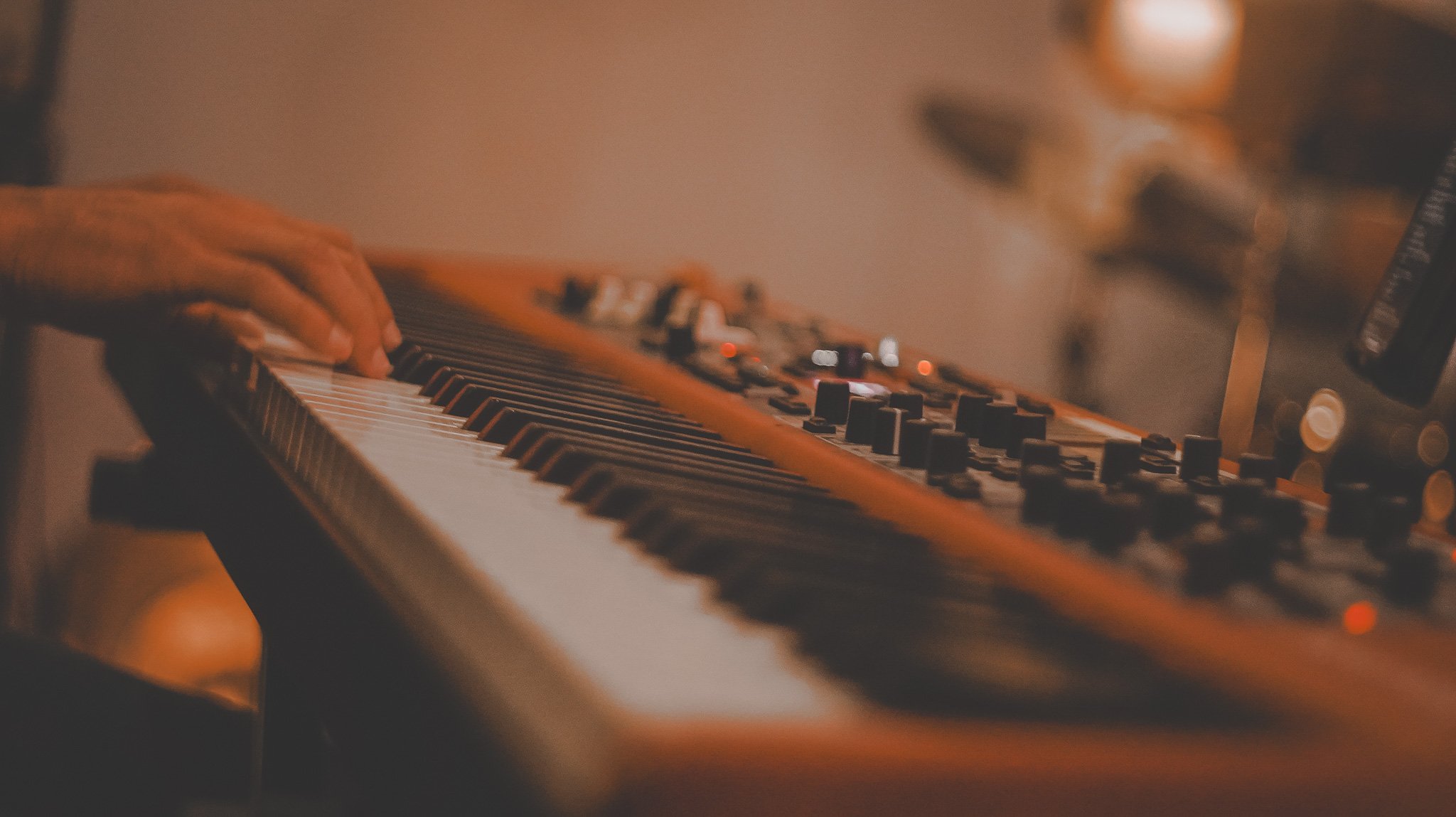 Close-up of a person's hand playing a synthesizer keyboard in a dimly lit room.