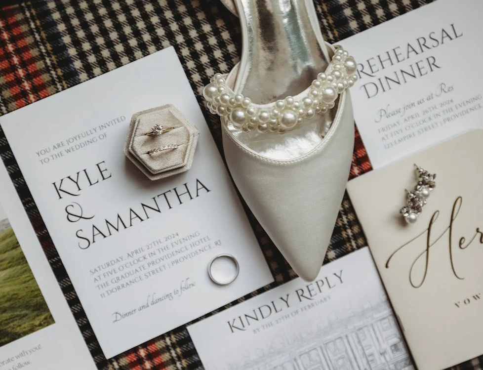 Wedding invitation, diamond rings, pearl necklace, and other wedding accessories on a tartan fabric background for wedding at The Graduate in Providence, Rhode Island.