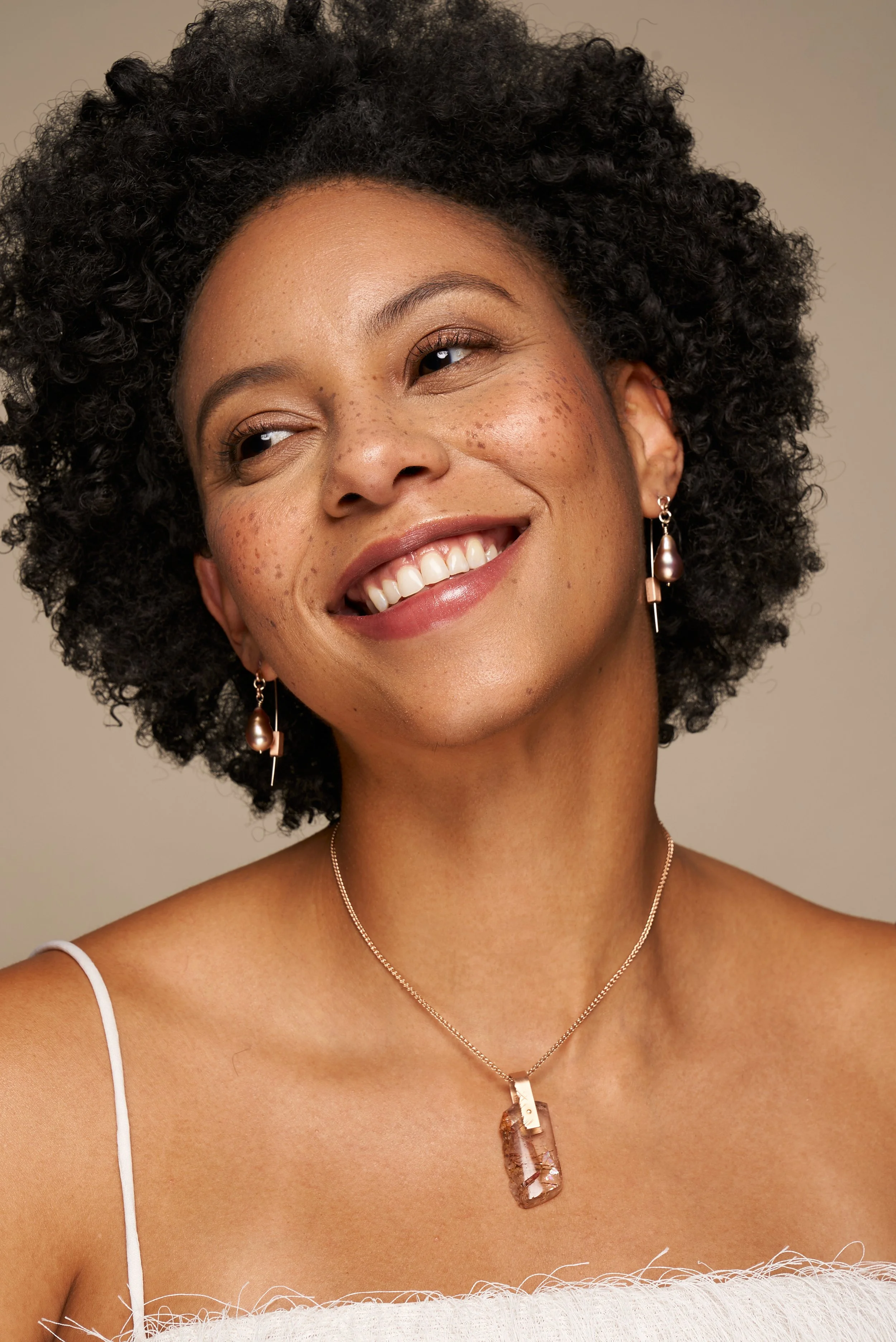 A smiling woman with curly black hair, wearing earrings and a necklace with a rectangular pendant.