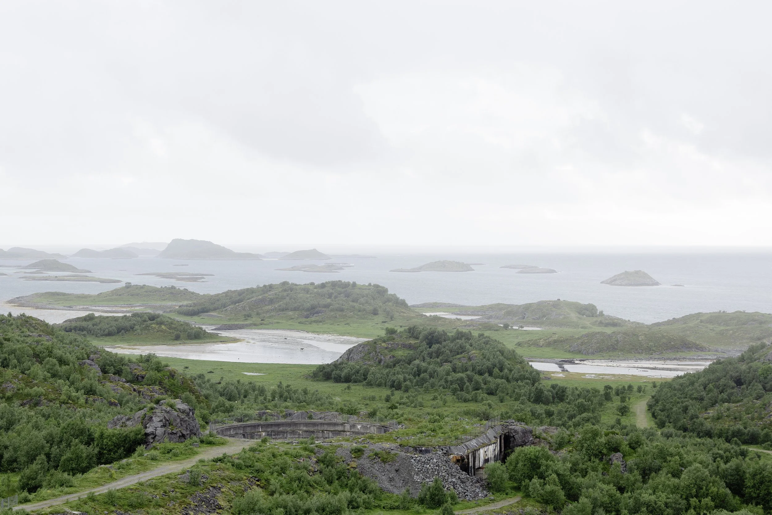 Elv og grønt land med et vann, flere øyer og en, uklar værhimmel
