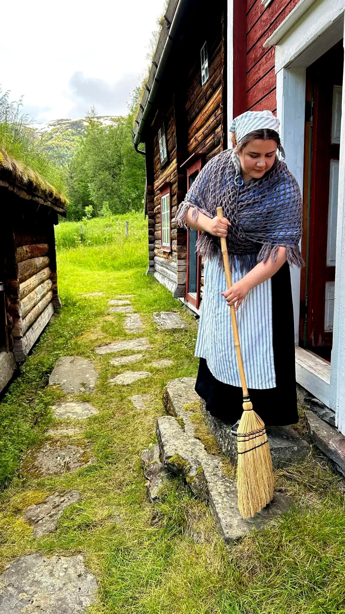 Foto einer Frau in altmodischer Kleidung, die eine Treppe fegt.