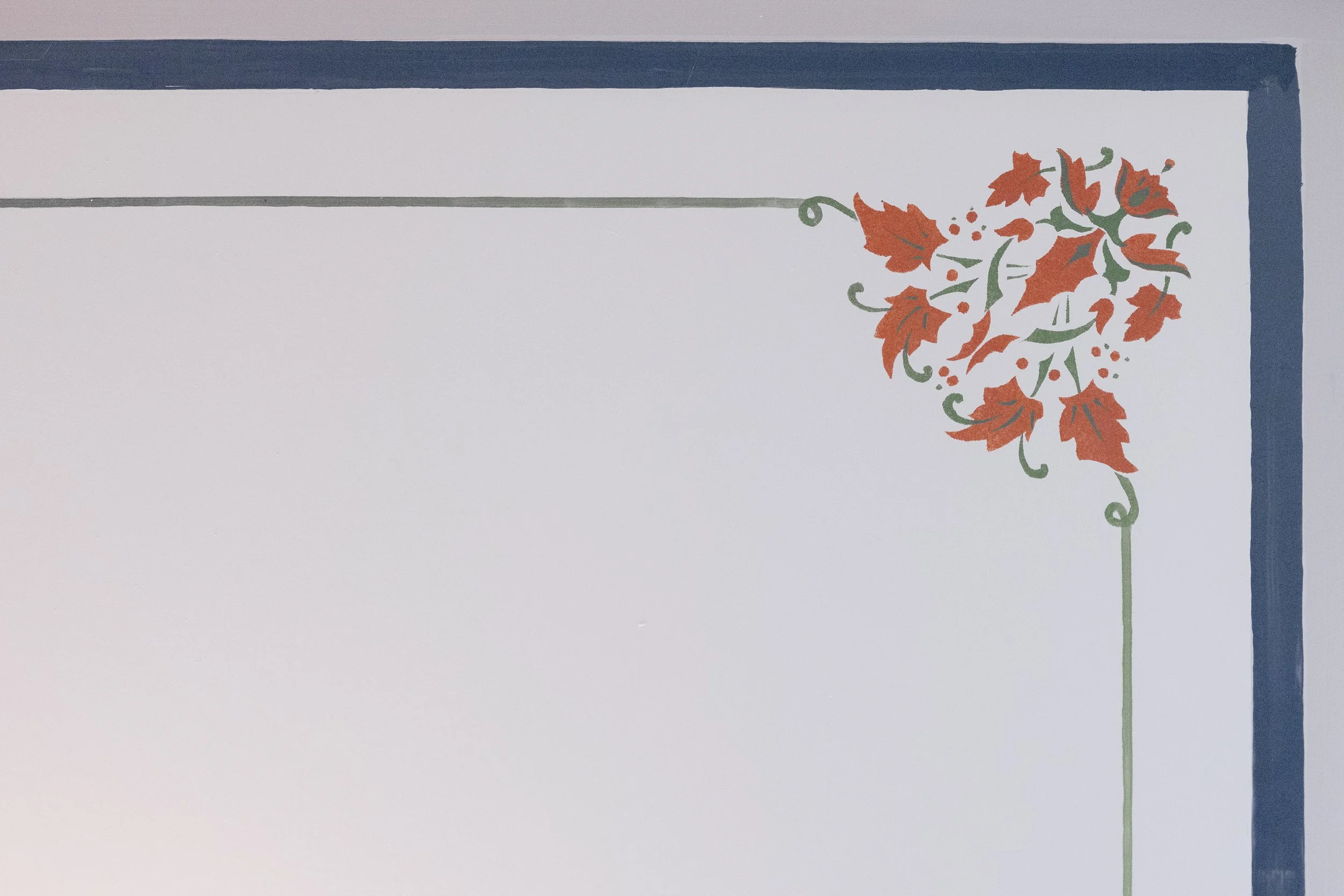 En hvit vegg med dekorative malte blader og blomster i rødt og grønt, omgitt av en mørk blå ramme.
