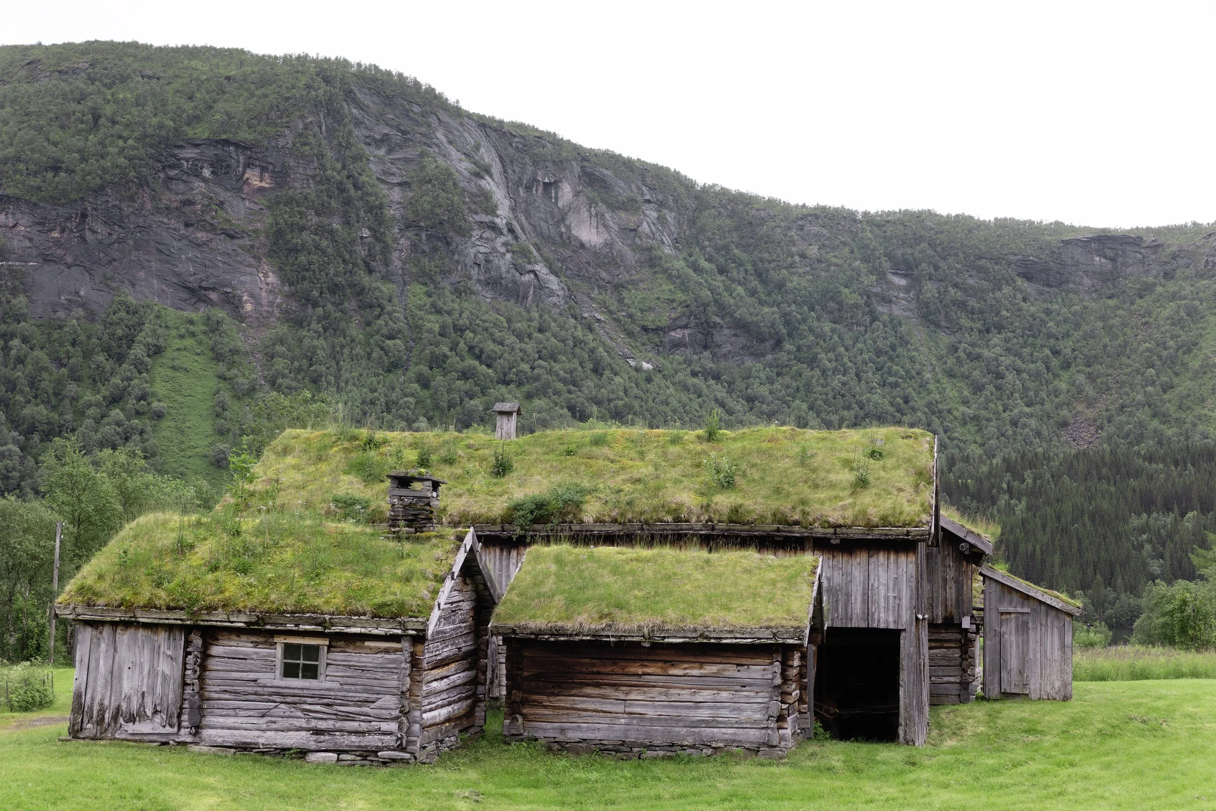 Hytter langs en innsjø omgitt av grønne trær og fjell