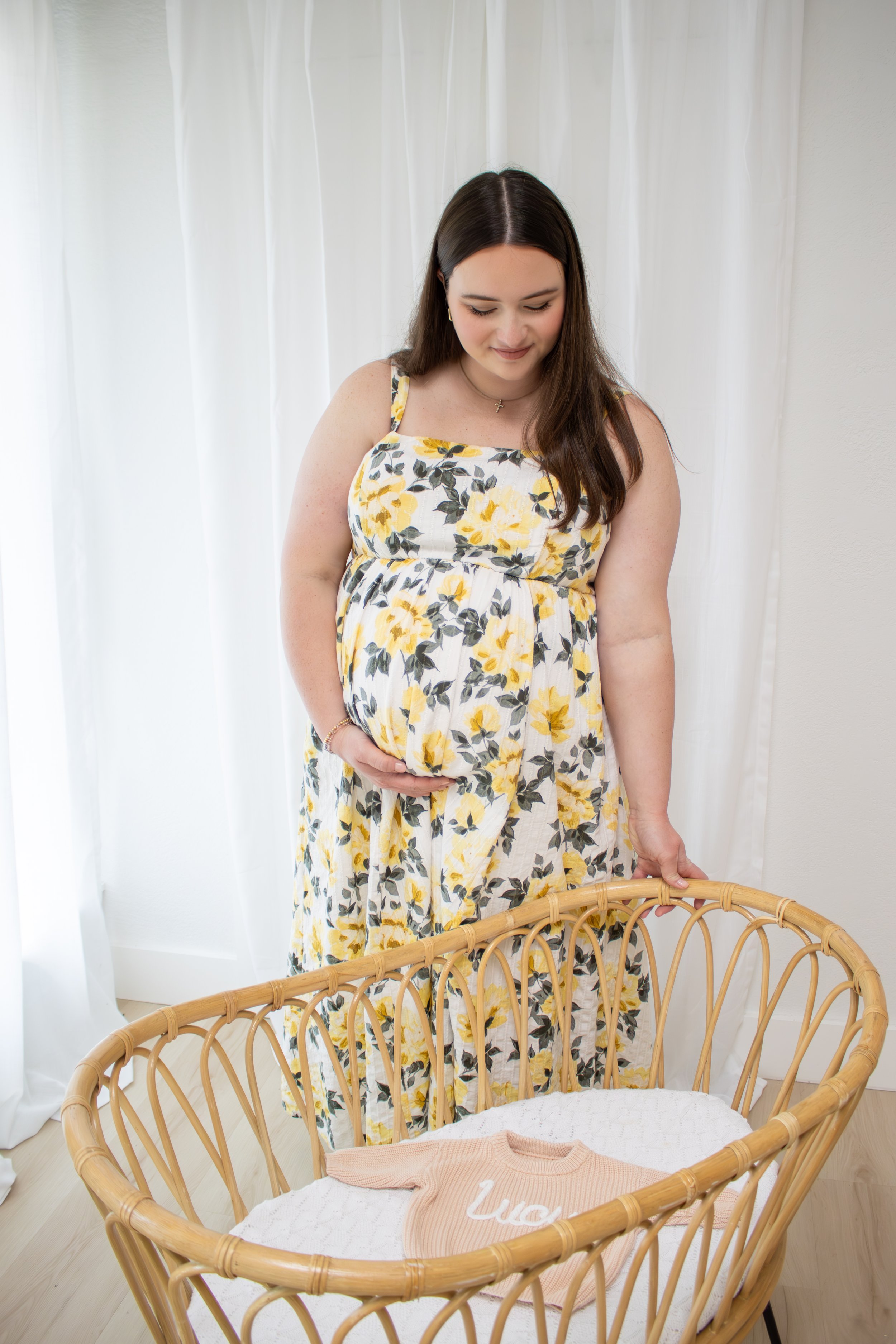 A pregnant woman in a pink dress smiling and posing against a white wall.