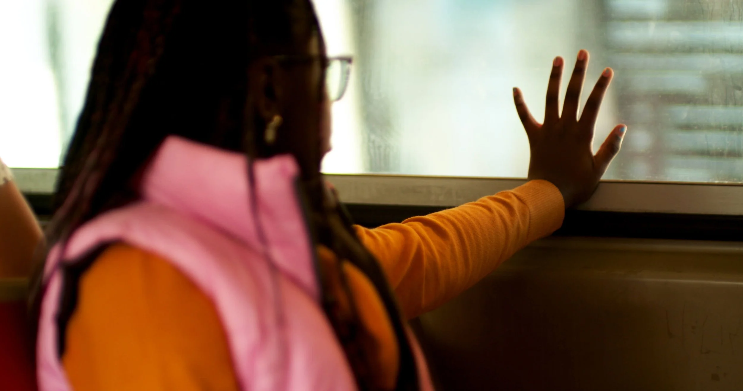 Person in a pink vest with an orange sleeve, reaching their hand towards a window.