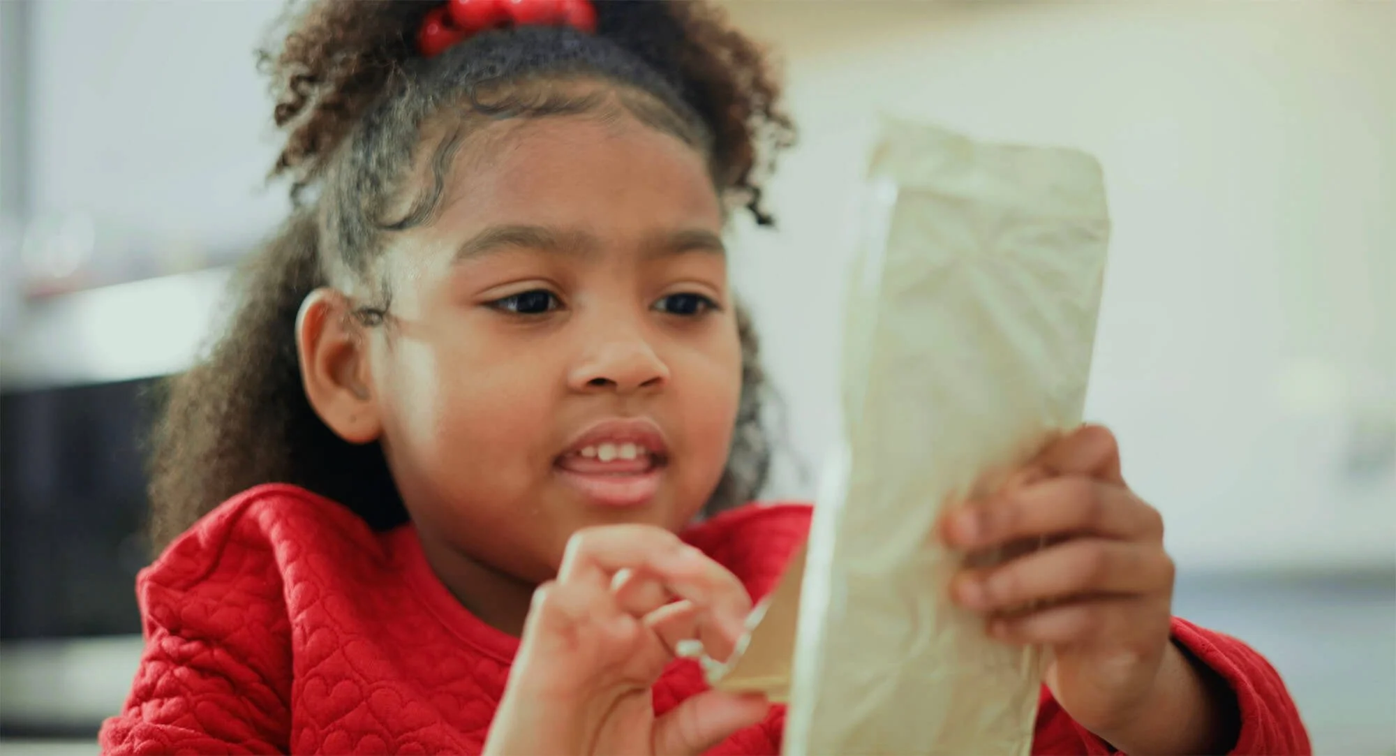 Young girl in a red shirt holding a piece of paper, looking at it closely.
