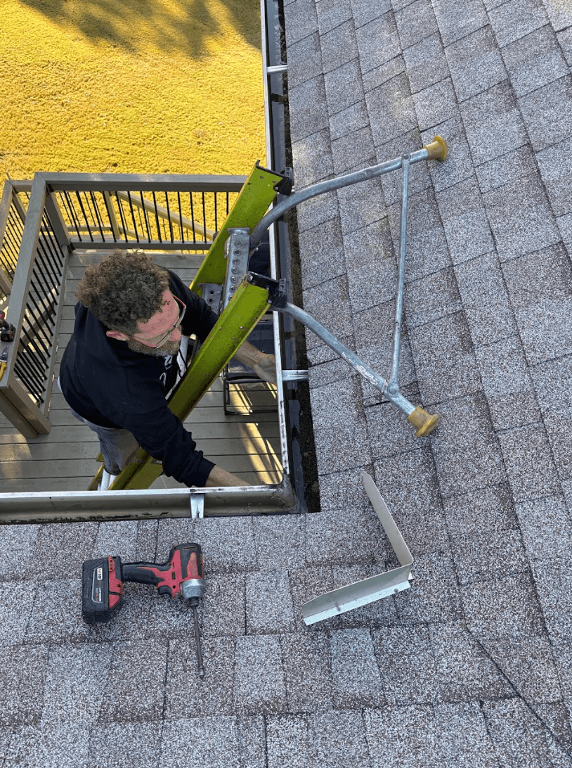 Worker on a ladder installing gutters along a residential roof with tools visible, Chattanooga, Tennessee