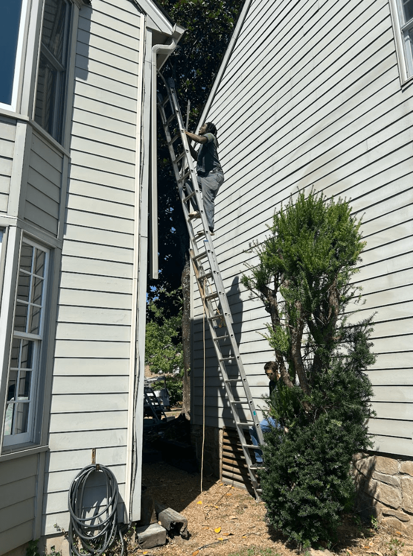 Technician on a ladder cleaning gutters on a two-story residential home exterior in Chattanooga, Tennessee