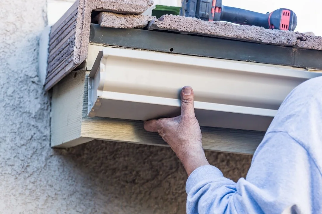 A close-up of a gutter technician’s hand precisely fitting a new section of almond-colored seamless aluminum guttering onto a residential roofline in Chattanooga.