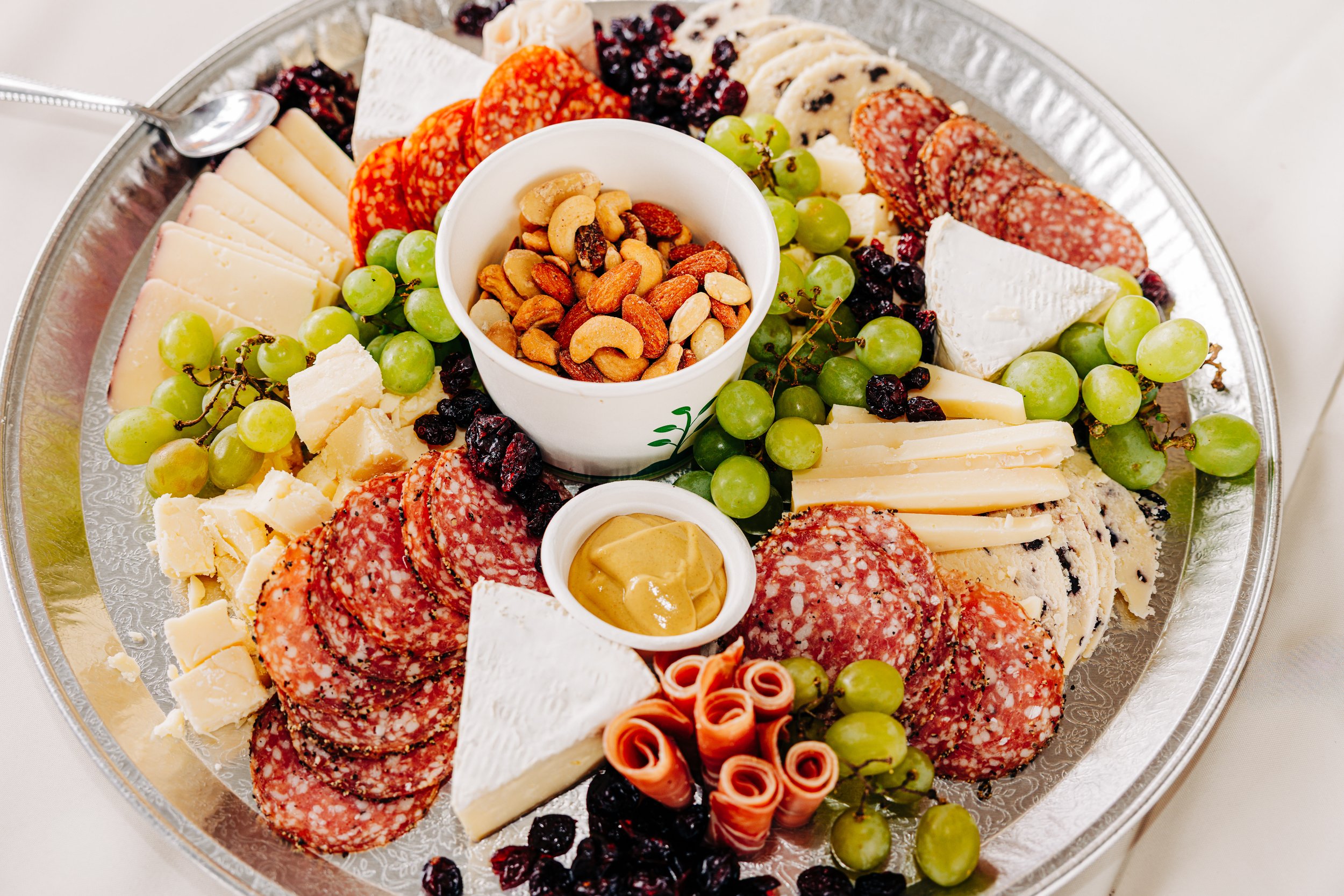 A meat and cheese platter with grapes, nuts, and mustard.