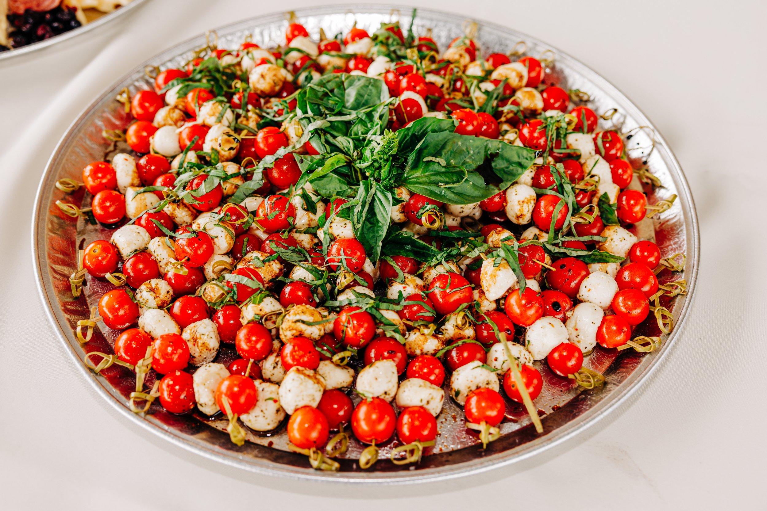 Tomato and mozzarella skewers with basil on a platter.