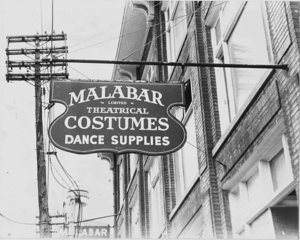 Sign for Malabar Limited Theatre, advertising costumes and dance supplies, hanging on a building in an urban area.