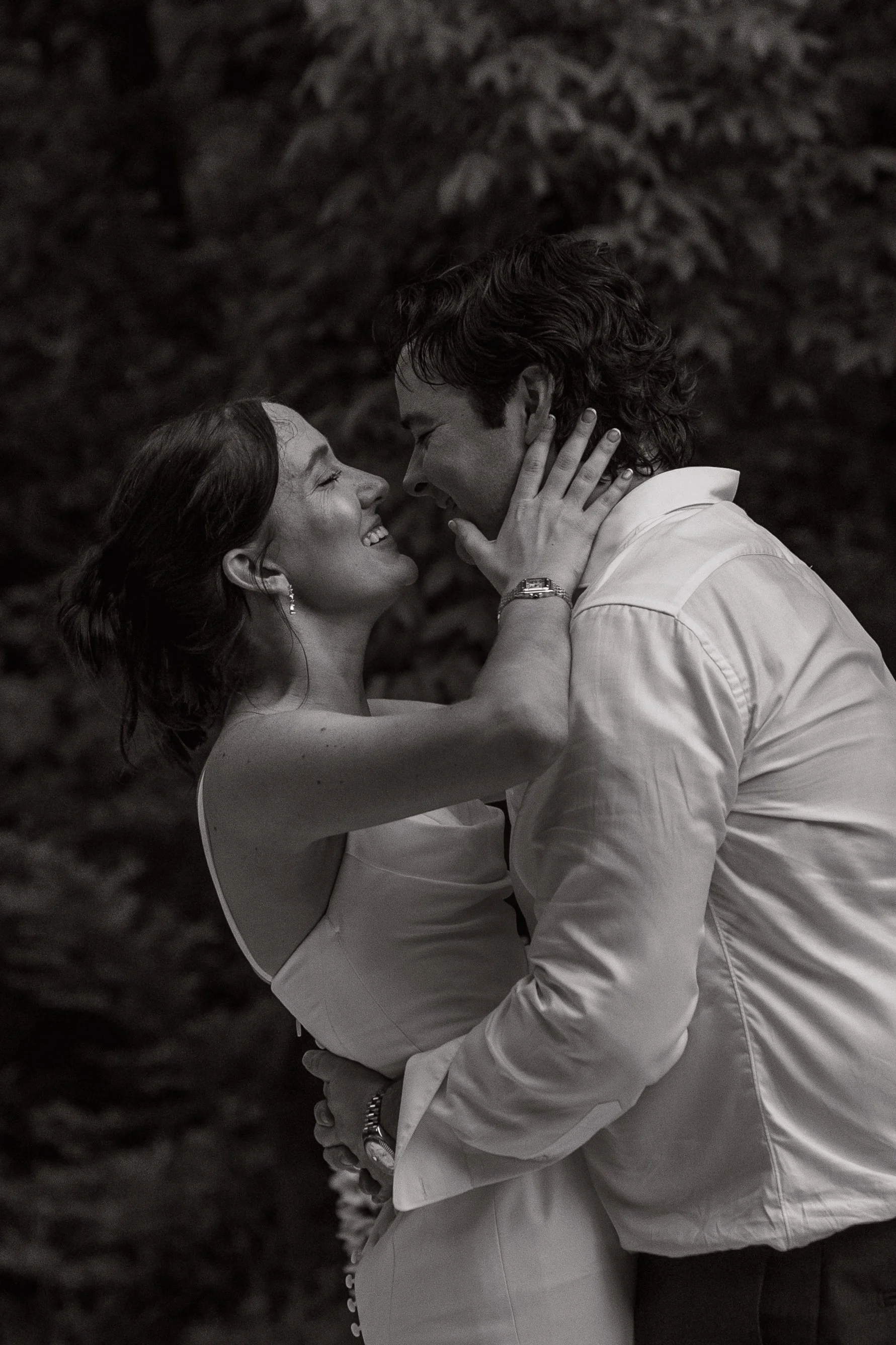 black and white image of a bride and groom having a warm embrace during their last dance at the end of the evening, the grooms hands are around her waist, pulling her in as she cups his face with her hands, the both of them smiling with their faces a
