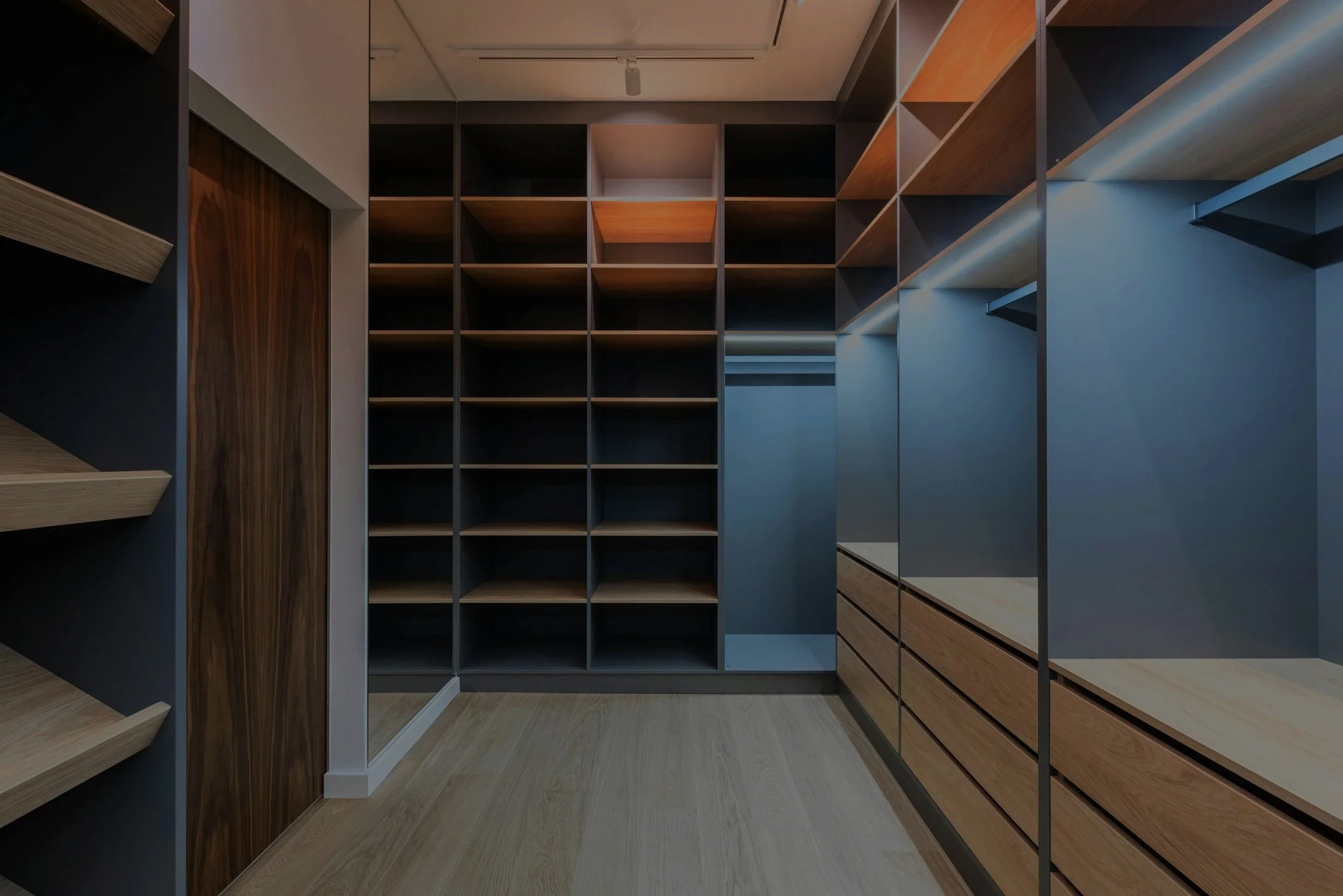 A walk-in closet with wooden shelves and hanging racks containing neatly organized clothing, boxes, and accessories