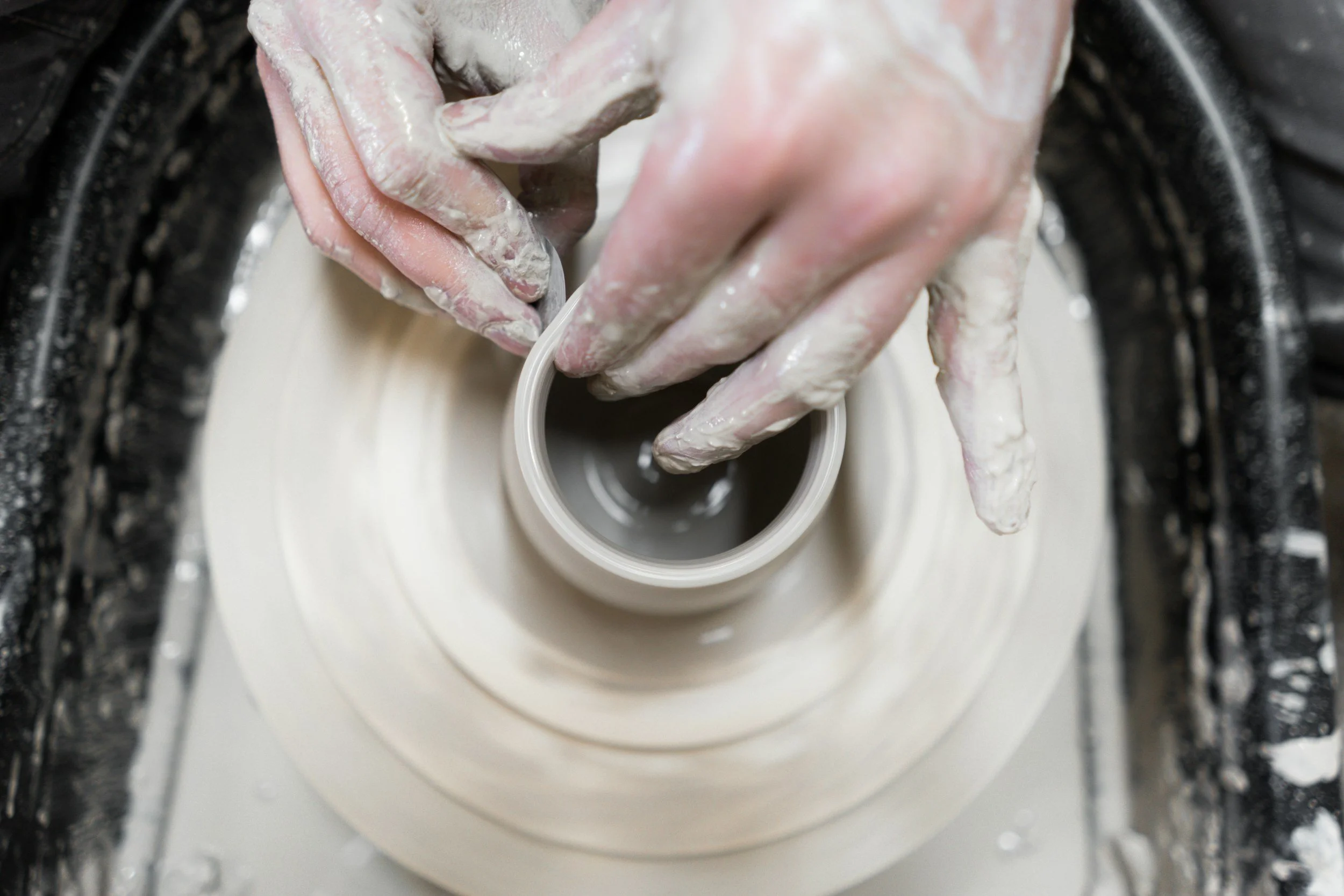 Hands shaping a piece of clay on a pottery wheel.