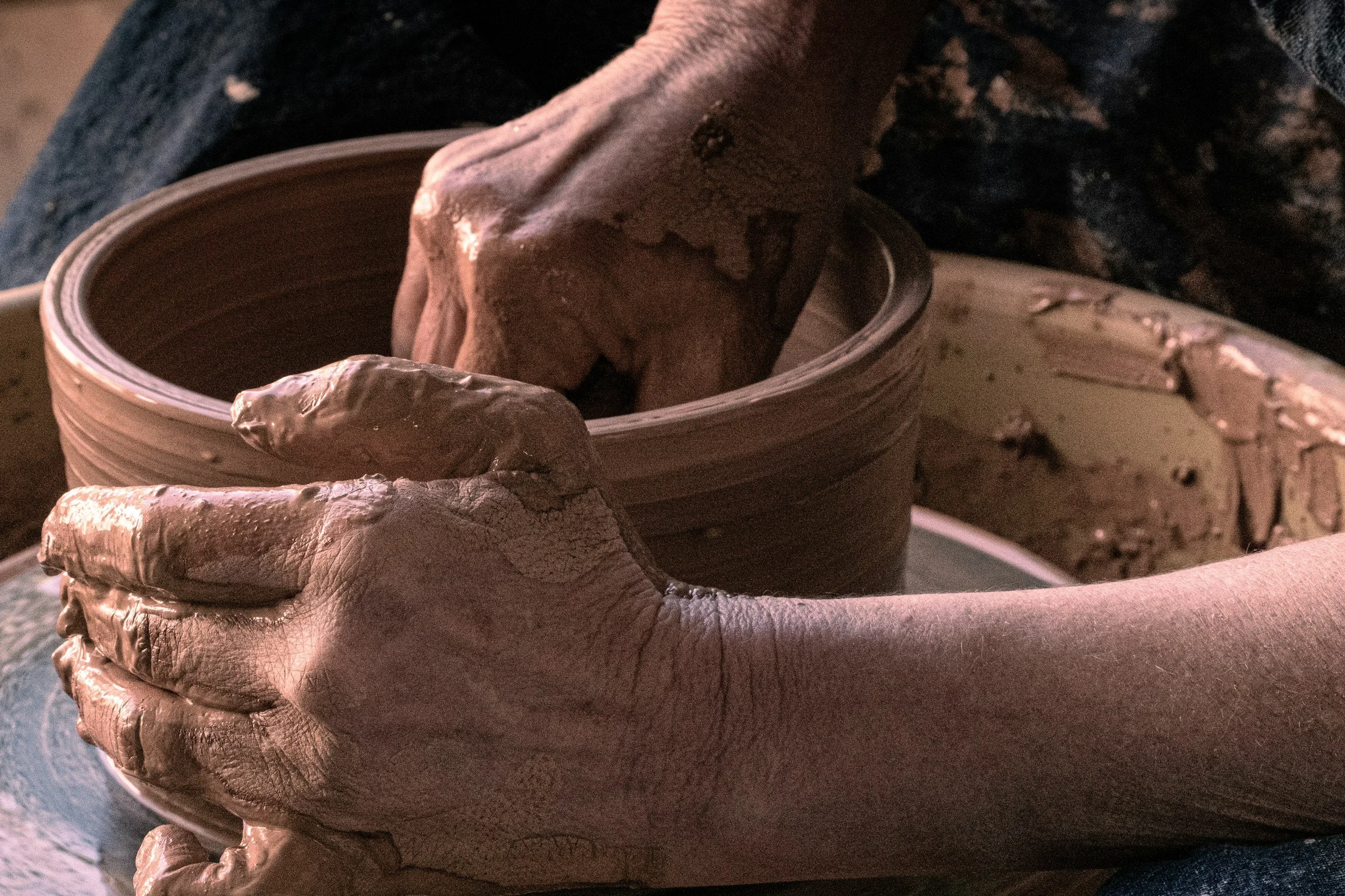 Close-up of a person's hands shaping a clay pot on a pottery wheel.