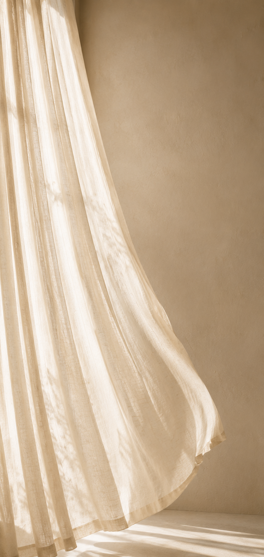 Soft, sheer linen curtain gently billowing in warm natural light against a textured beige wall, creating a calm, minimalist atmosphere.