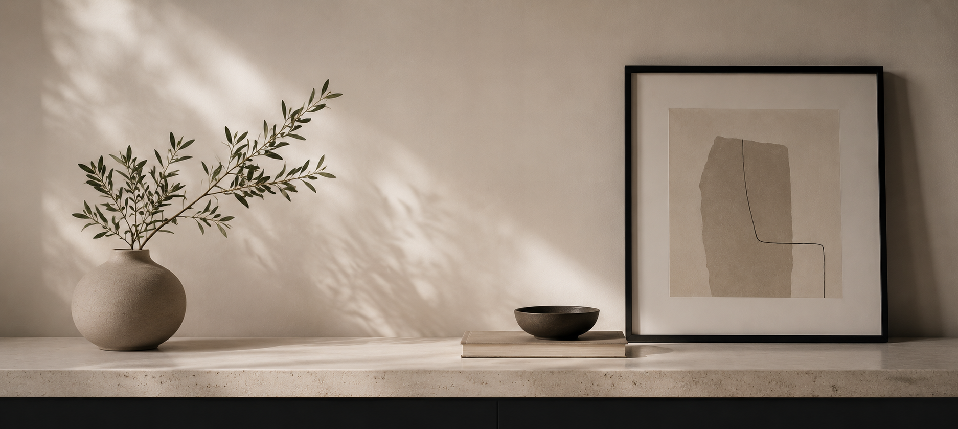 Minimalist interior scene with a ceramic vase holding a leafy branch, soft natural light casting shadows on a neutral wall, and a framed abstract artwork resting on a console.