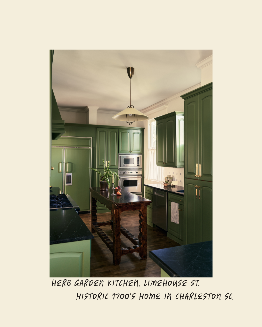 A kitchen with green cabinets, black countertops, and a wooden island with decorative carvings, featuring a potted herb on it. There is a vintage-style ceiling lamp, a window with curtains, and modern stainless steel appliances in a historic home in Charleston, South Carolina.