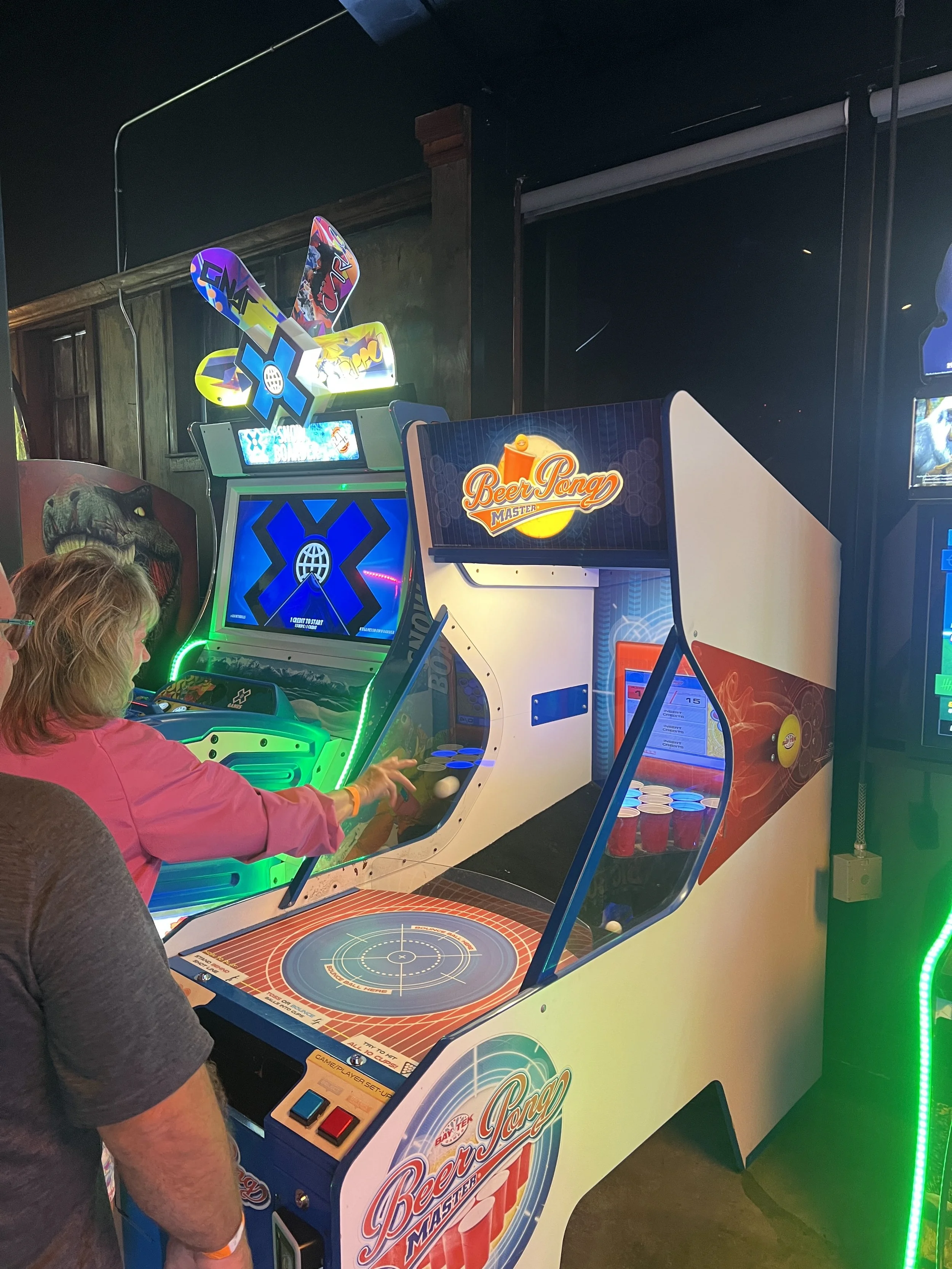 A woman playing an arcade game named Beer Pong in an arcade at Nowhere Entertainment with neon lights around her