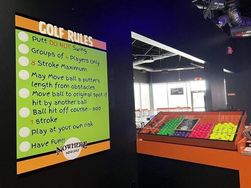 A neon green sign with orange sign showing the rules for mini golf at a mini golf course in Inver Grove Heights