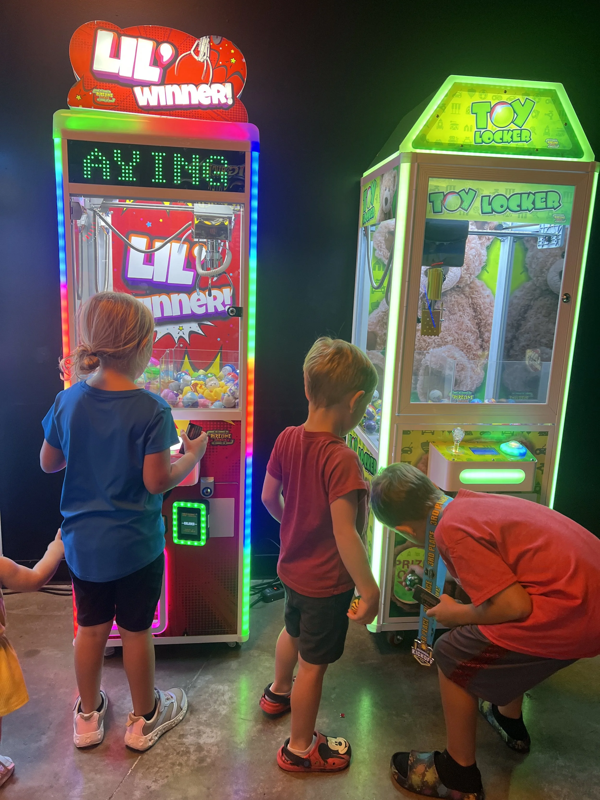 Three young boys playing on neon colored crane machine games in an arcade at Nowhere Entertainment in Inver Grove Heights